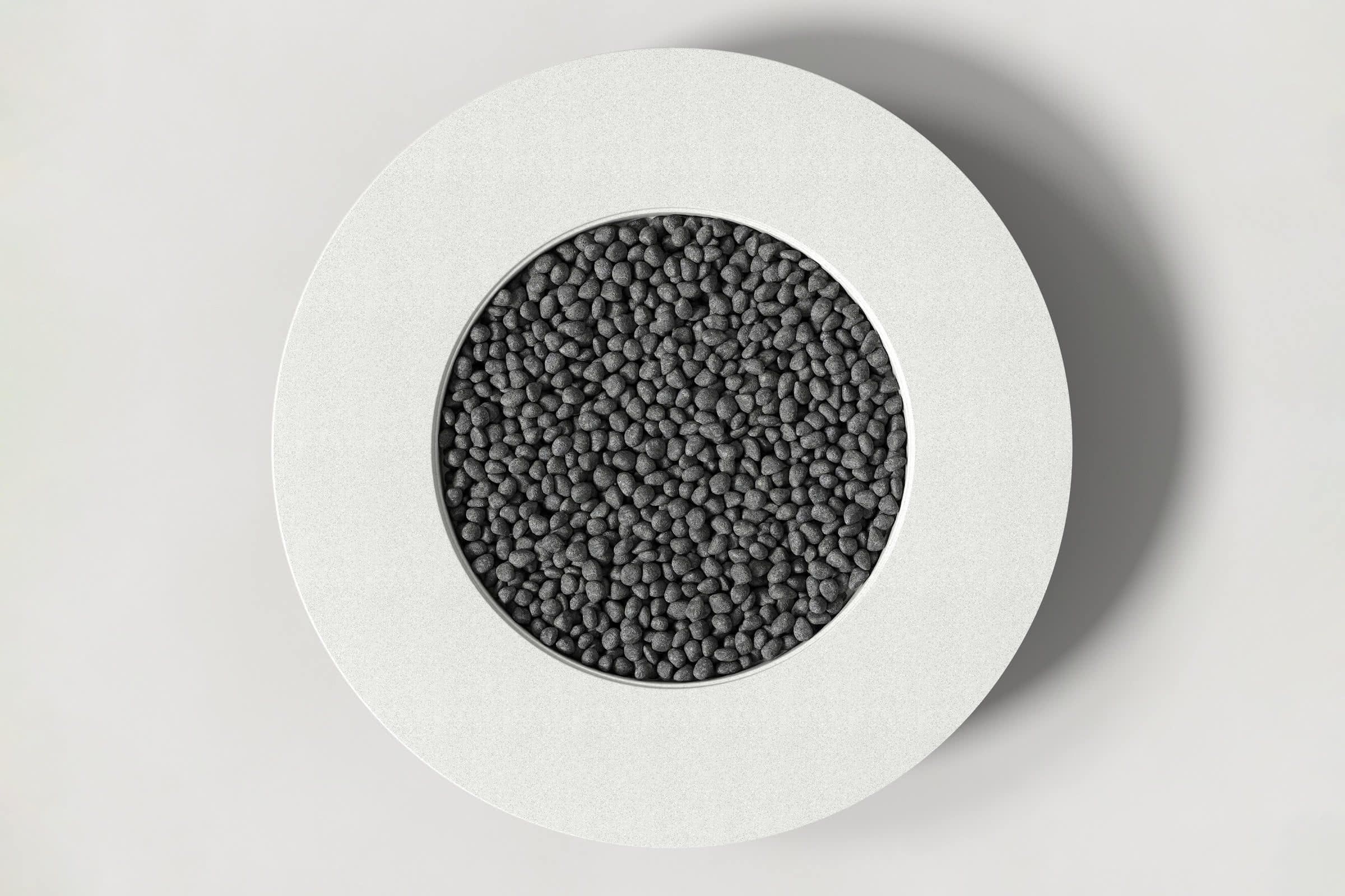 Top-down view of a circular white concrete fire pit with thick walls and a circular well filled with volcanic rocks. Shown against a white background with slight shadows.
