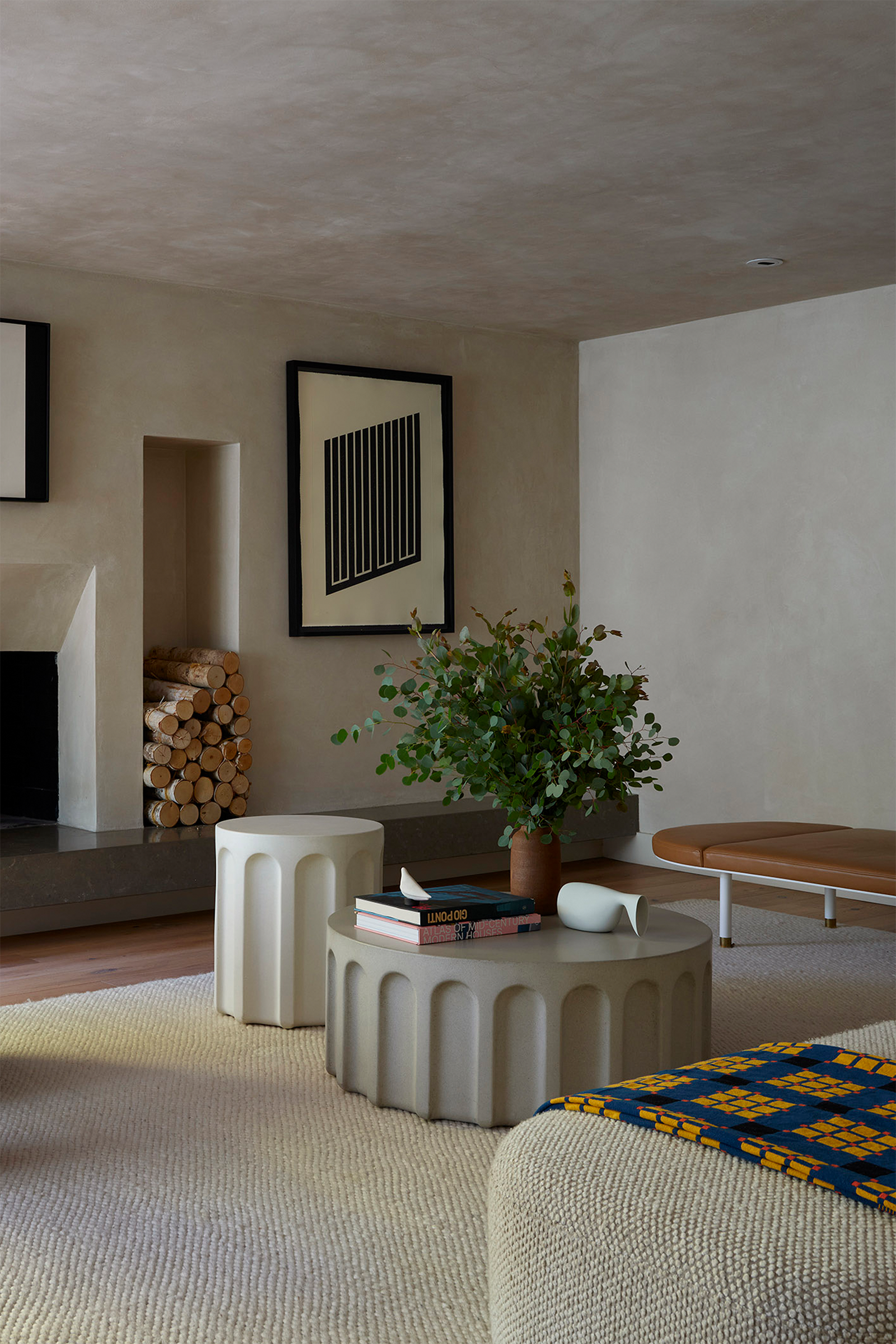 Contemporary living room with fluted white concrete tables, geometric art, green accent chair and built-in fireplace. Light wood floors, cream run and plaster walls.