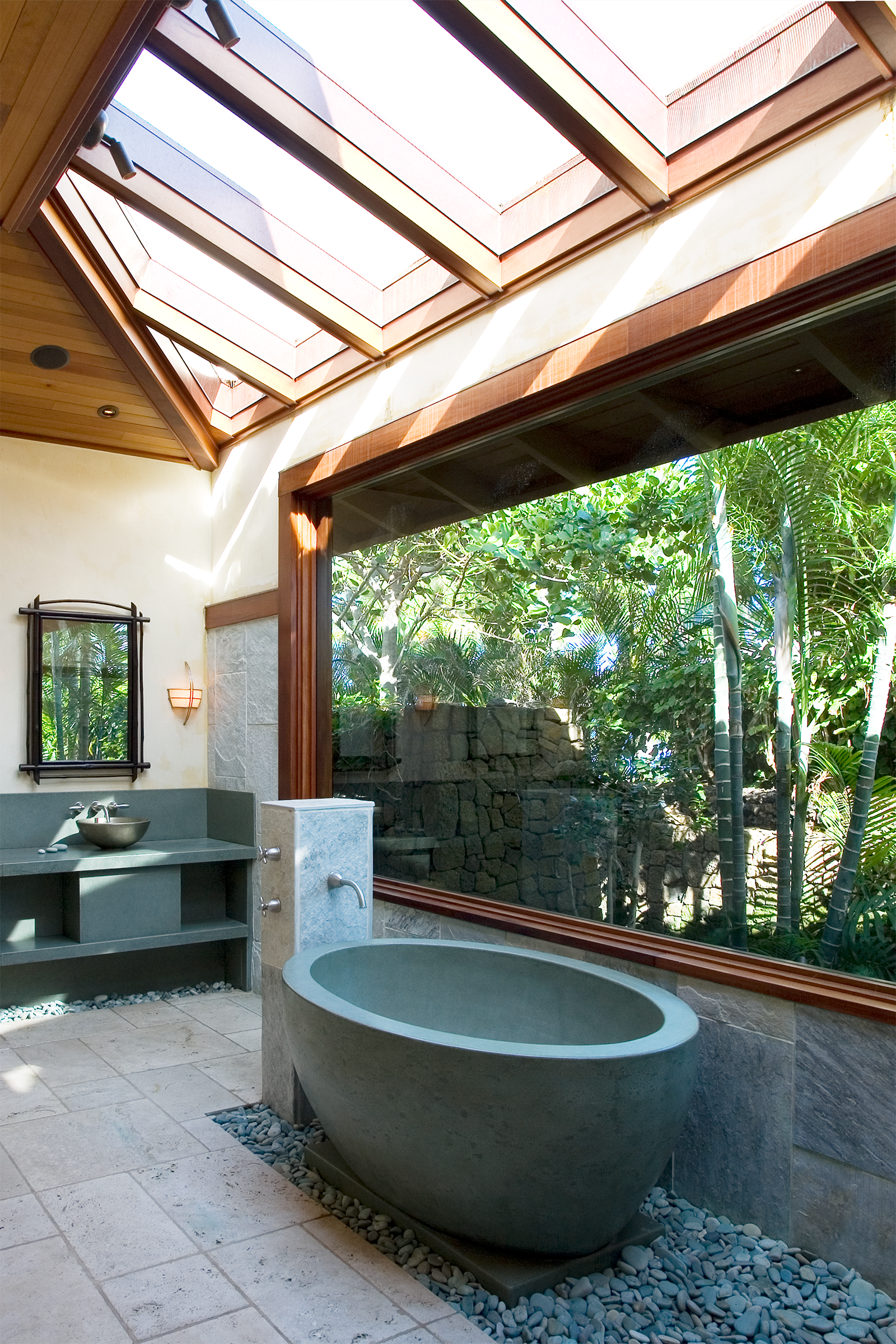 Compact grey concrete bathtub, with a curved form in a resort placed on top of stones. The background shows natural lighting with greenery.