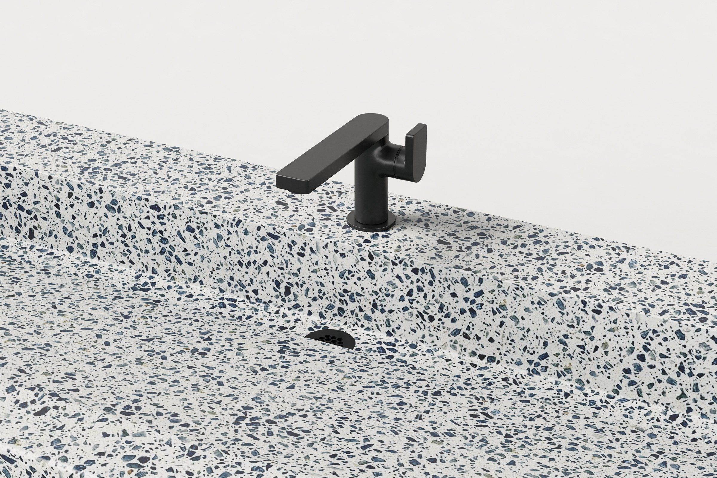 Detail view of Unazzo terrazzo Trof sink with matte black faucet and sloped basin geometry.