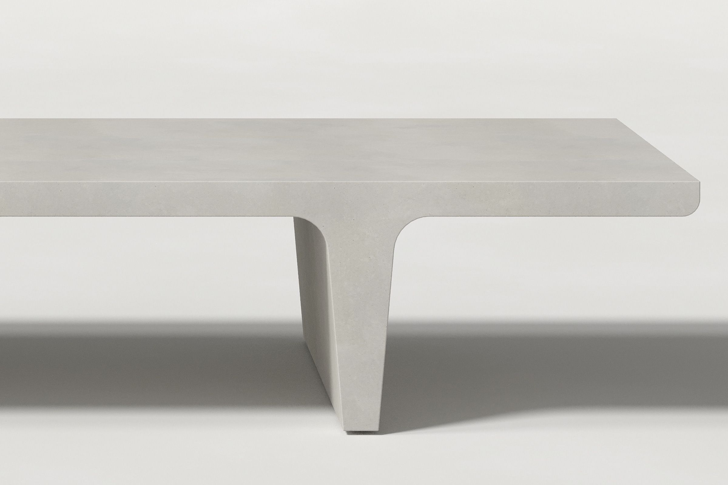Close-up of a light grey concrete coffee table with sculptural double tee legs, highlighting soft edges and subtle surface texture against a clean white background.