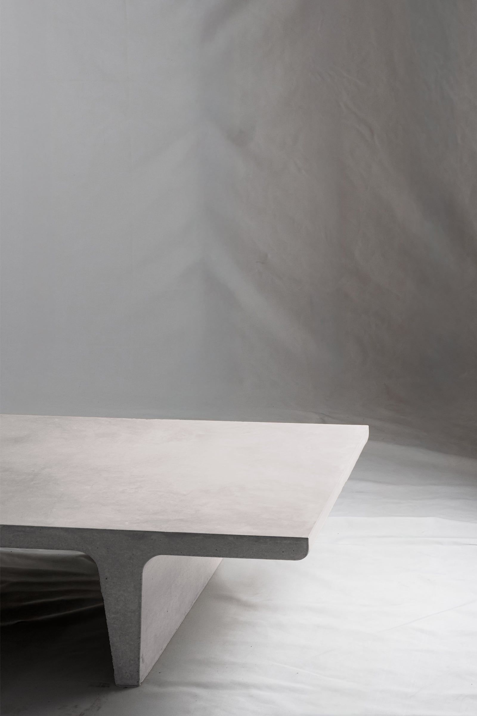 A close up of a light grey concrete coffee table with sculptural double tee legs, featuring a smooth troweled finish, set against a soft neutral backdrop.