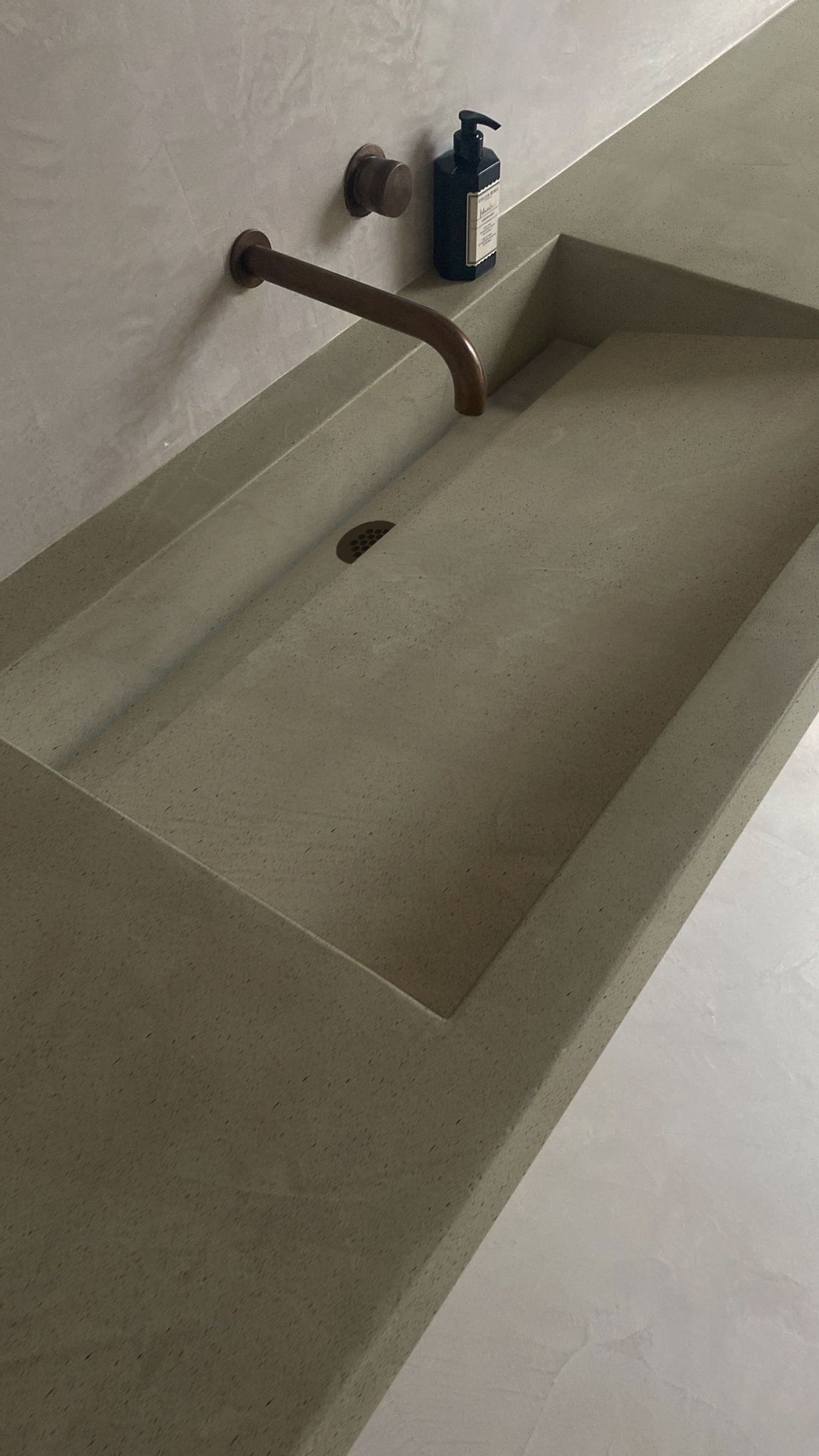 Minimalist concrete sink with wall-mounted faucet against a light plaster wall.