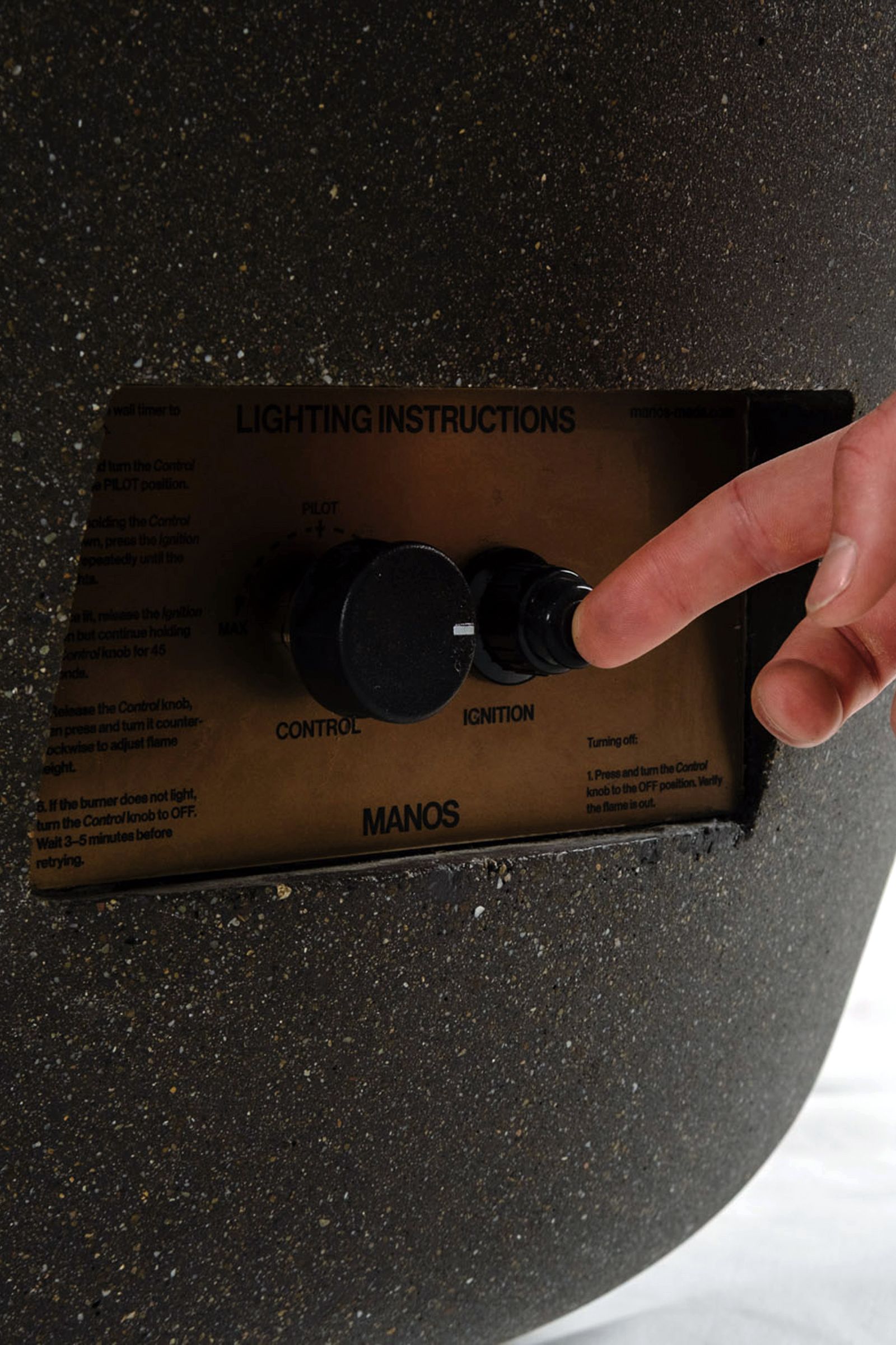 Close-up of lighting instructions and controls of the Rosa fire pit, a round dark grey concrete fire pit with etched sides.