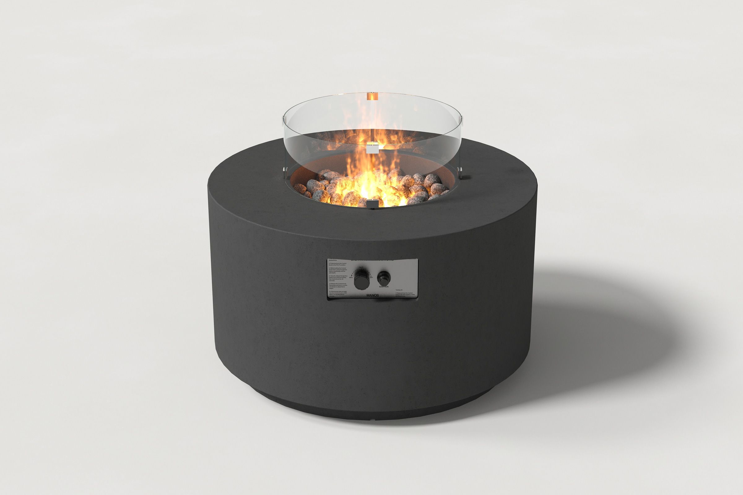 Low cylindrical charcoal colored concrete fire pit with thick walls and a central circular well filled with dark volcanic rocks and flame, with an integrated control panel, surrounded by a clear glass shield. Side view on a white background with a shadow to the right.