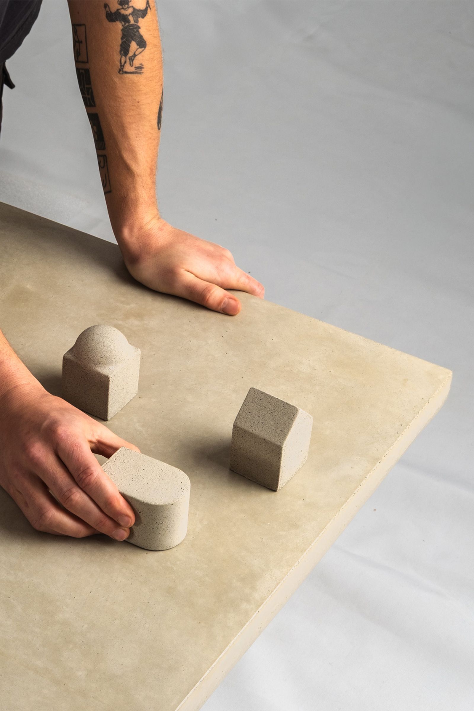 Close-up of a light beige concrete coffee table, showing hands arranging small concrete samples on the smooth surface.