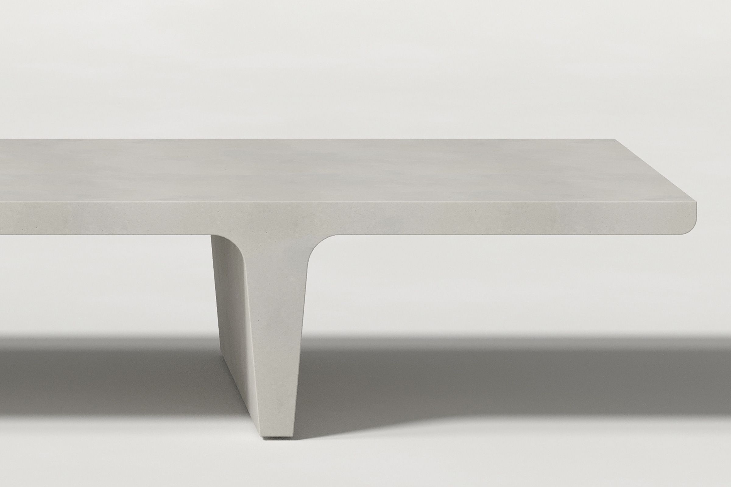 Close-up of a light grey concrete coffee table with sculptural double tee legs, highlighting soft edges and subtle surface texture against a clean white background.