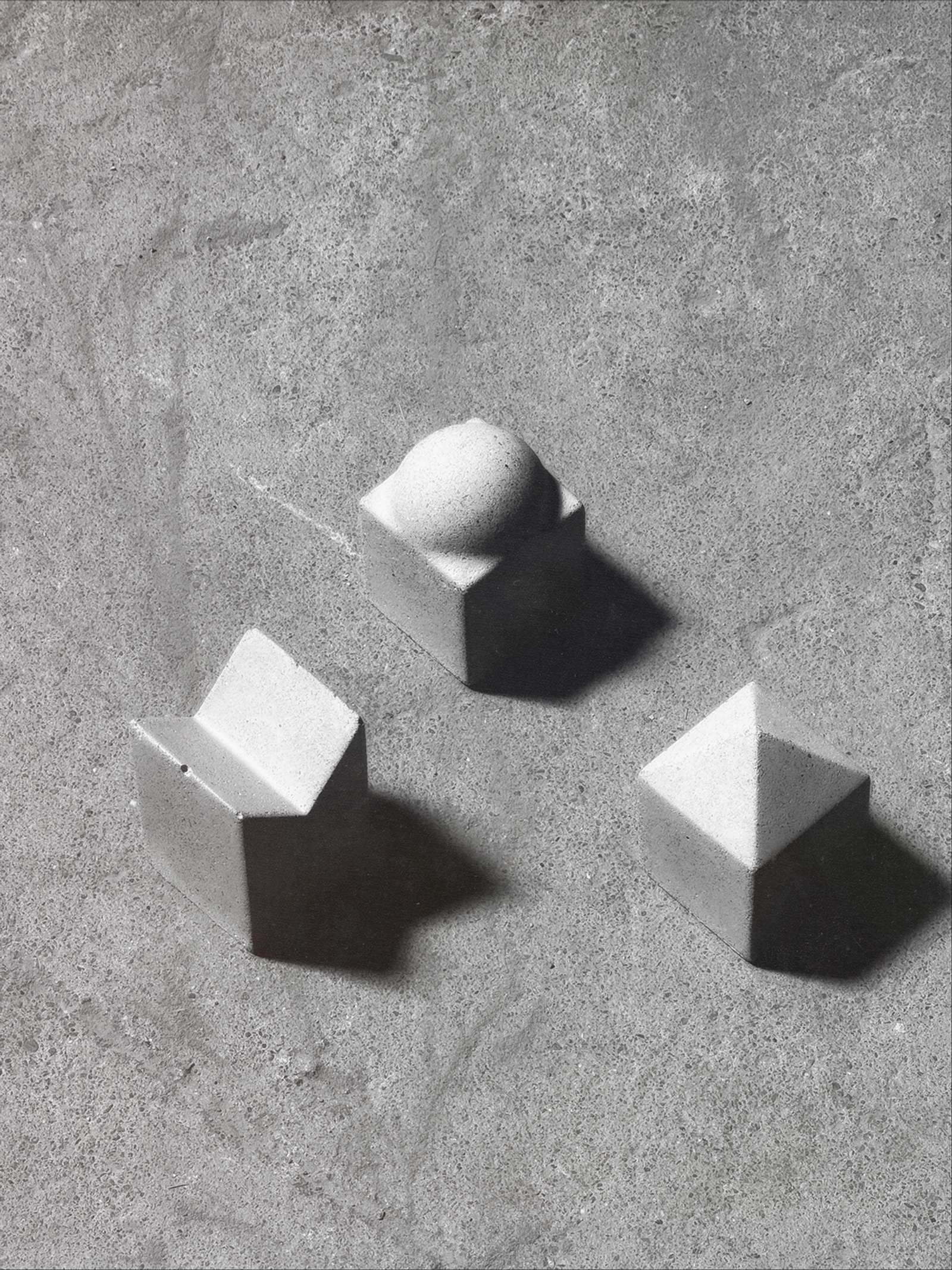 Three architecturally inspired, concrete objects on a concrete floor.