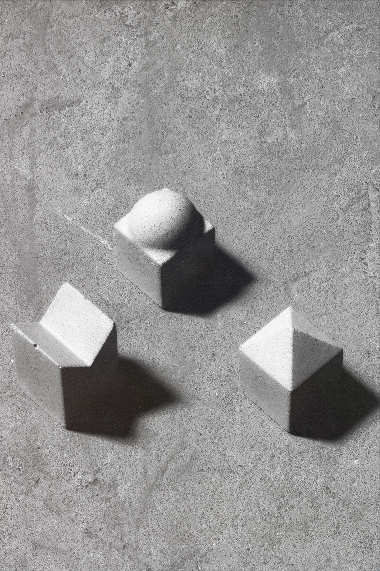 Three architecturally inspired, concrete objects on a concrete floor.