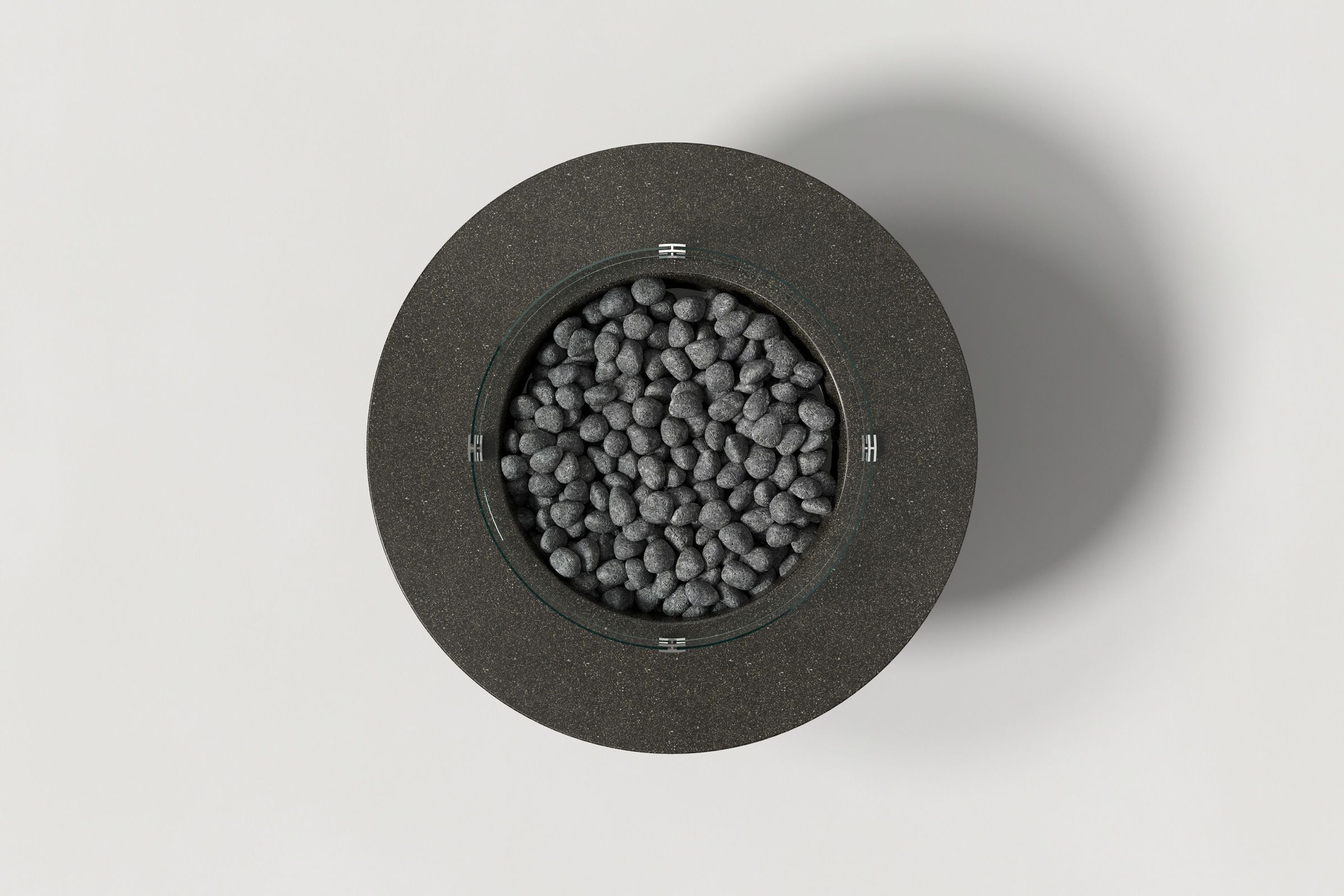 Top view of a round dark grey concrete fire pit with a honed top and etched sides, filled with lava rocks and surrounded by a circular glass shield, set against a clean white background.