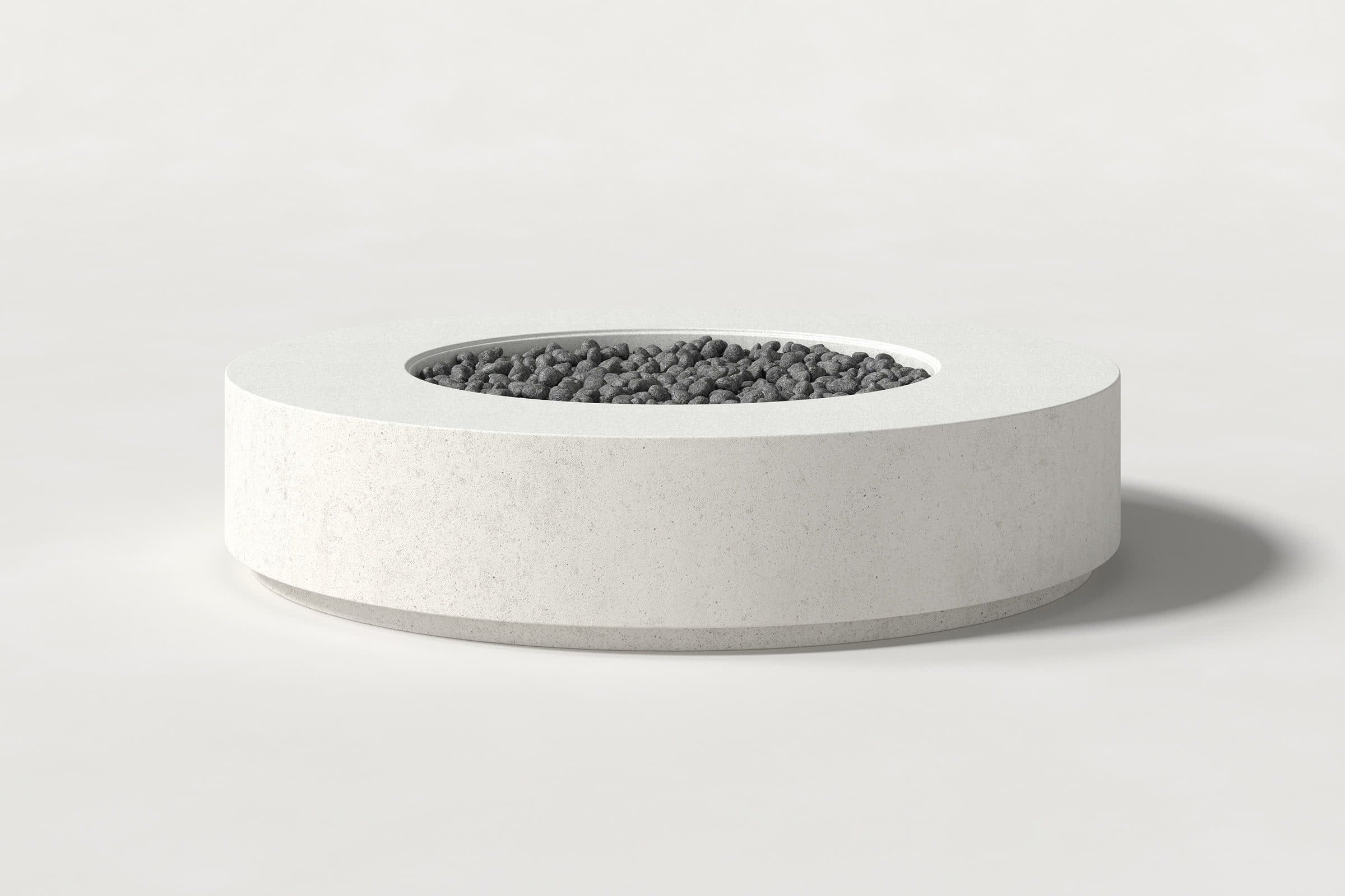 Low cylindrical white concrete fire pit with thick walls and a central circular well filled with dark volcanic rocks. Side view on a white background with a shadow to the right.