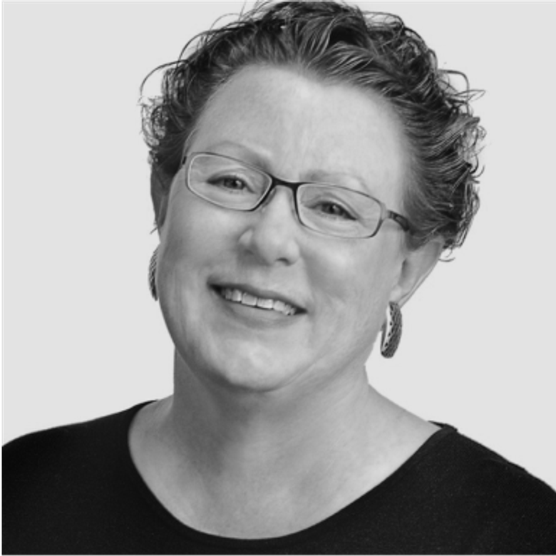 Black and white portrait of a person with curly hair and glasses wearing a dark top, smiling at the camera against a light background.