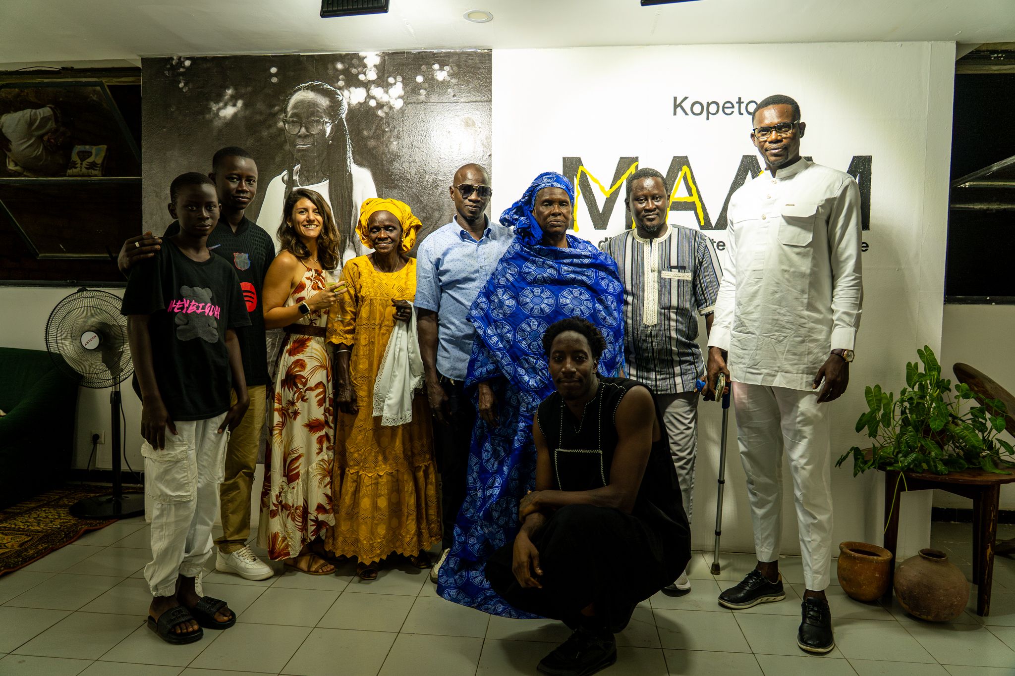 Kopeto, les MAAM et leurs familles posent devant le titre de l’exposition