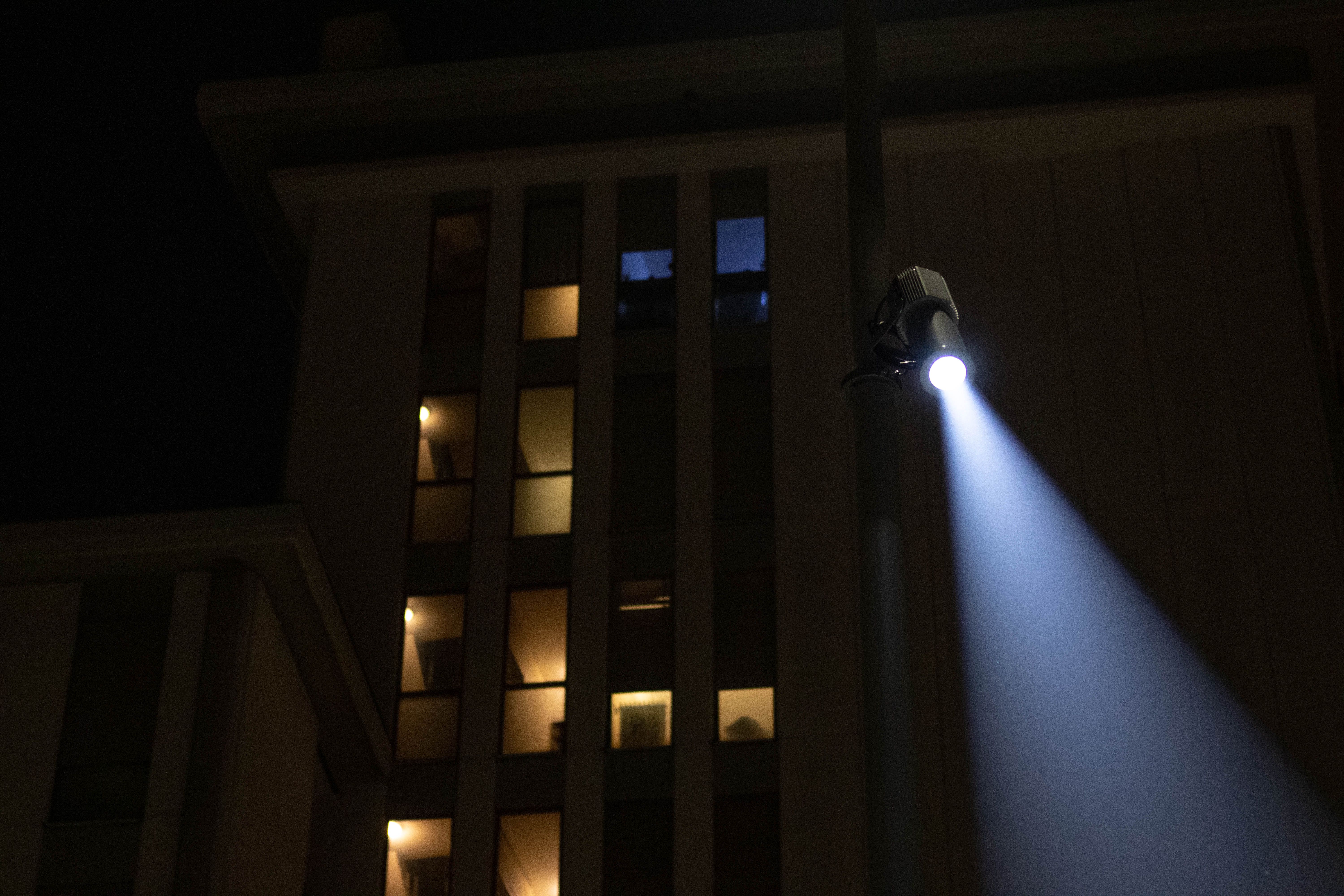 Stage light on a pole projecting a beam beside a building at night