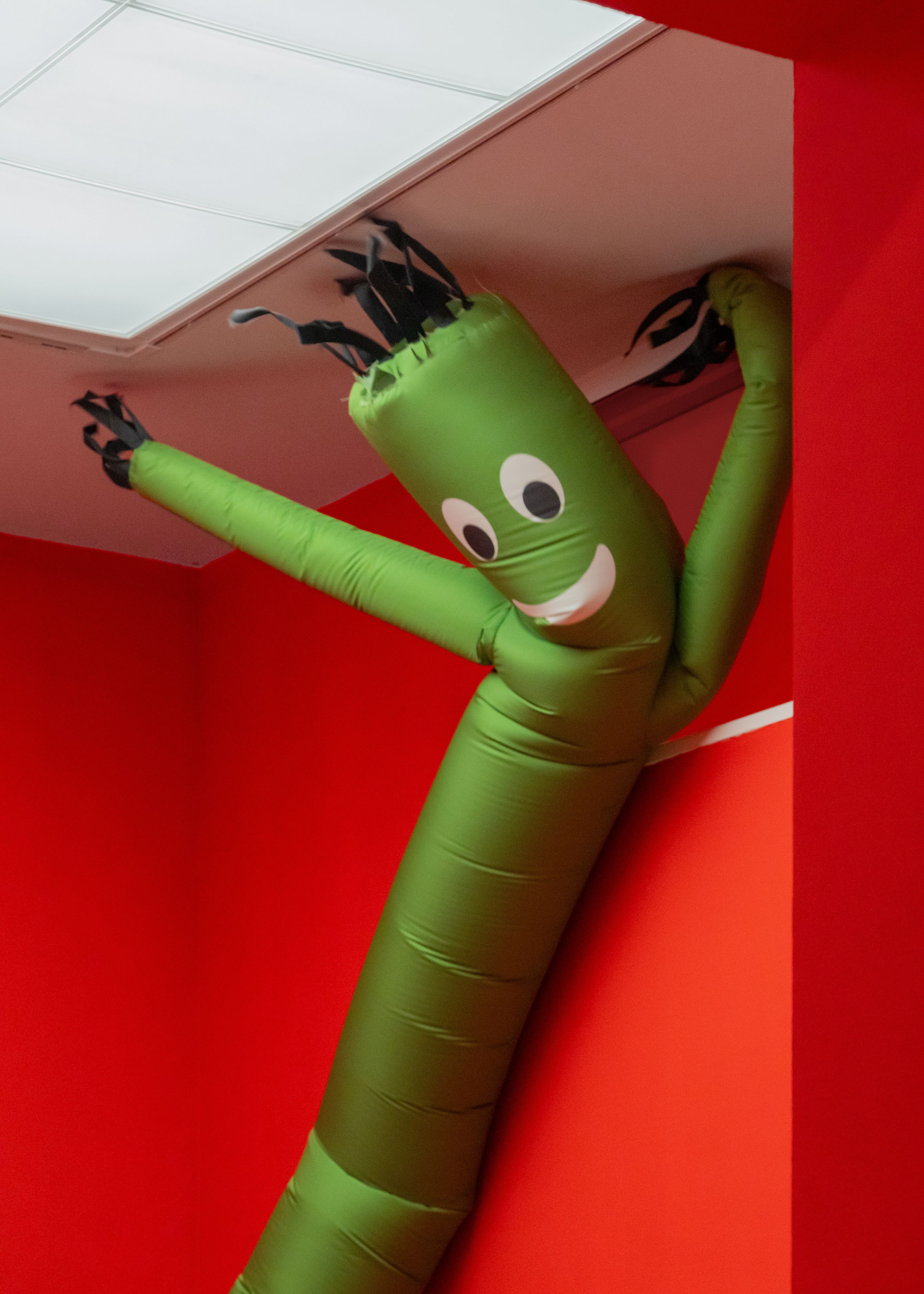 Green skydancer with a smiling face pressed against a red wall and ceiling