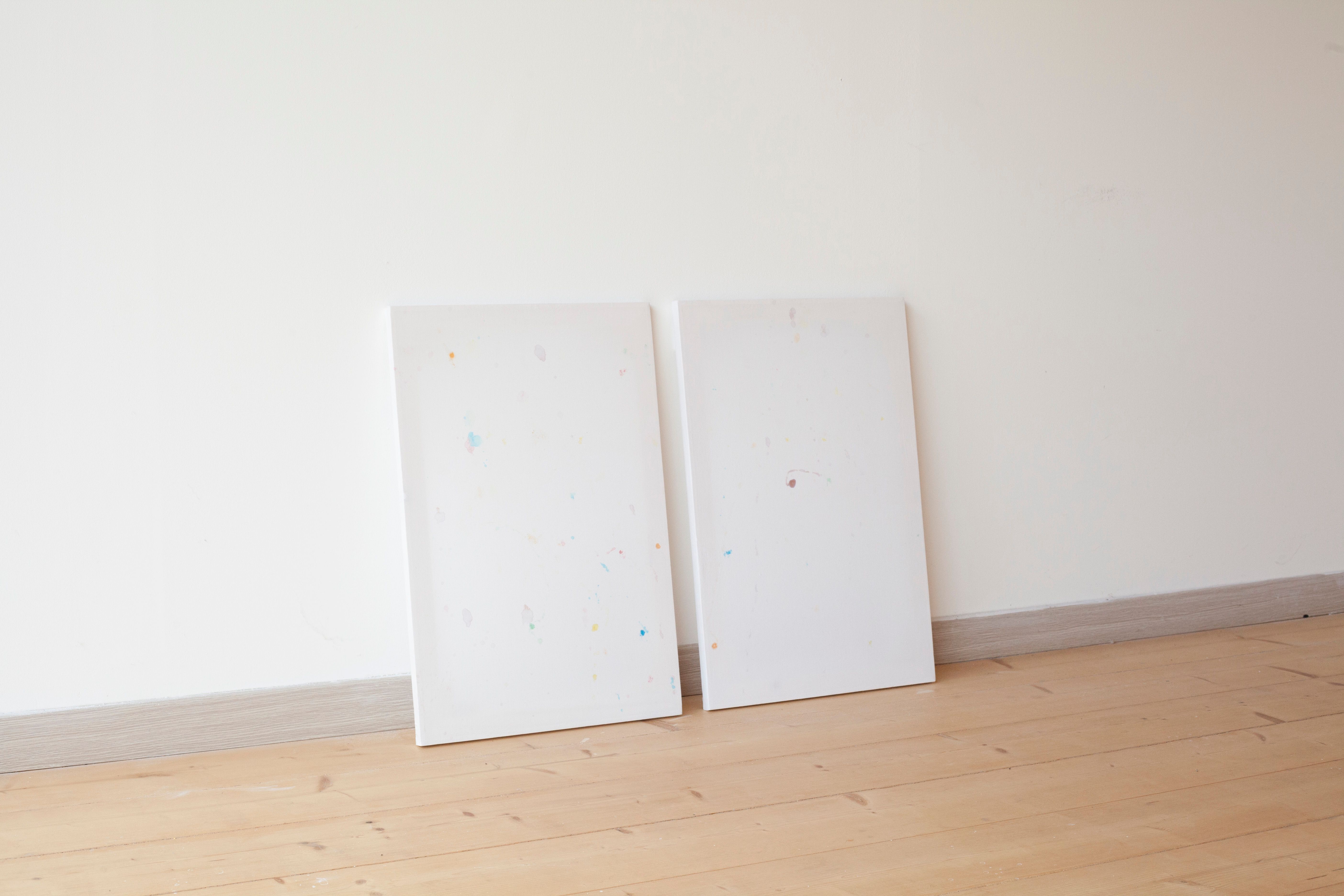 Two white sheets with faint coloured stains leaning against a wall on a wooden floor