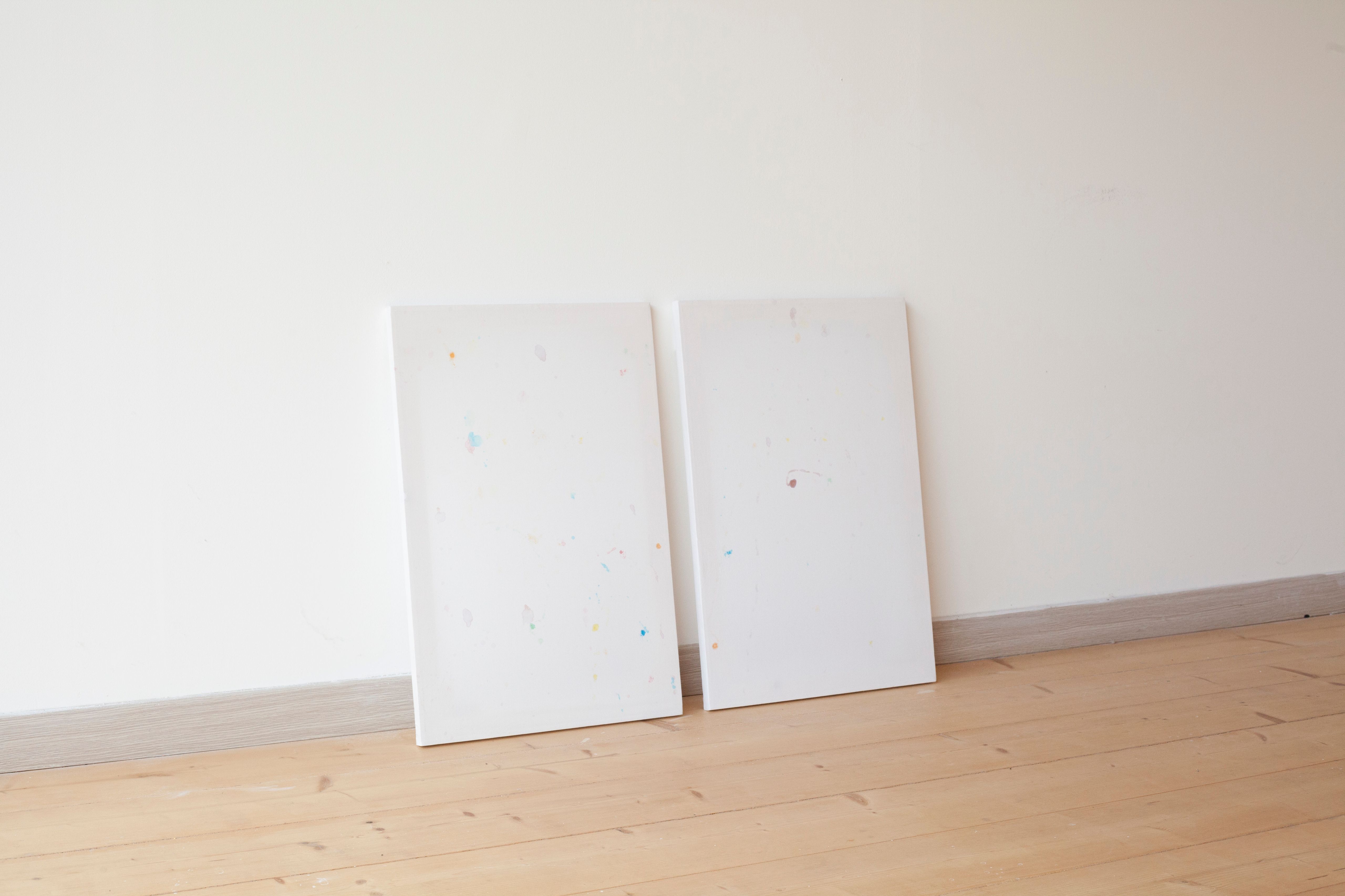 Two white sheets with faint coloured stains leaning against a wall on a wooden floor