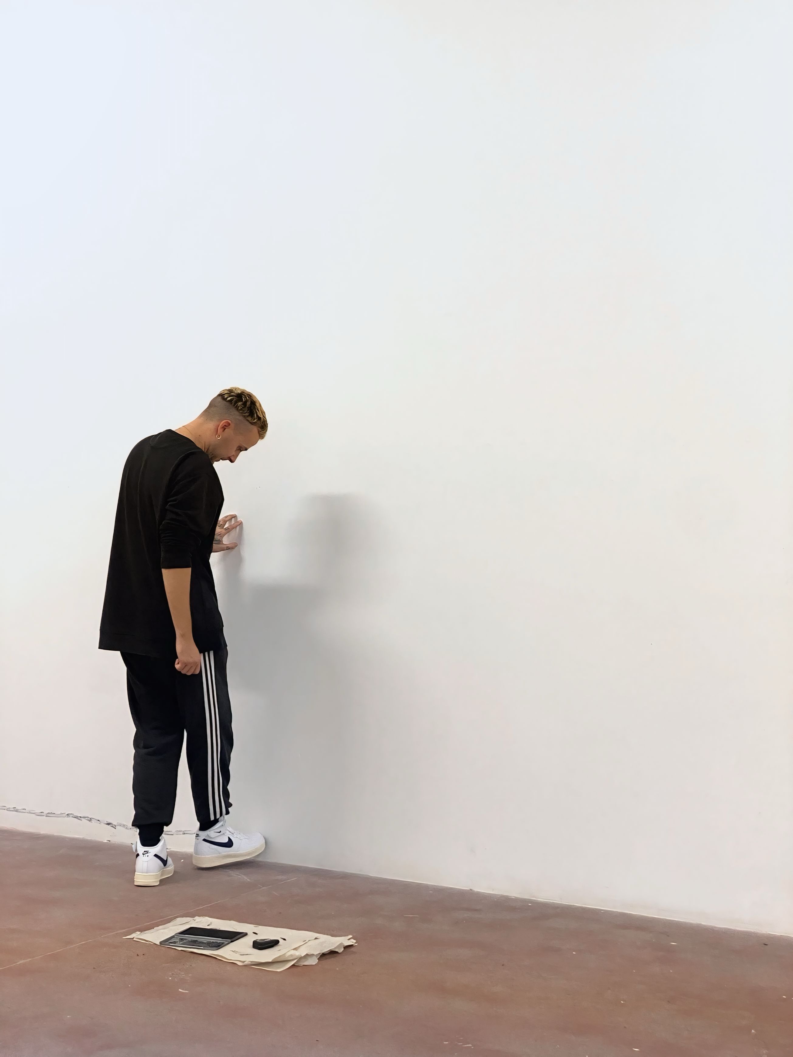 The artist kicking a white wall in a room with a red floor