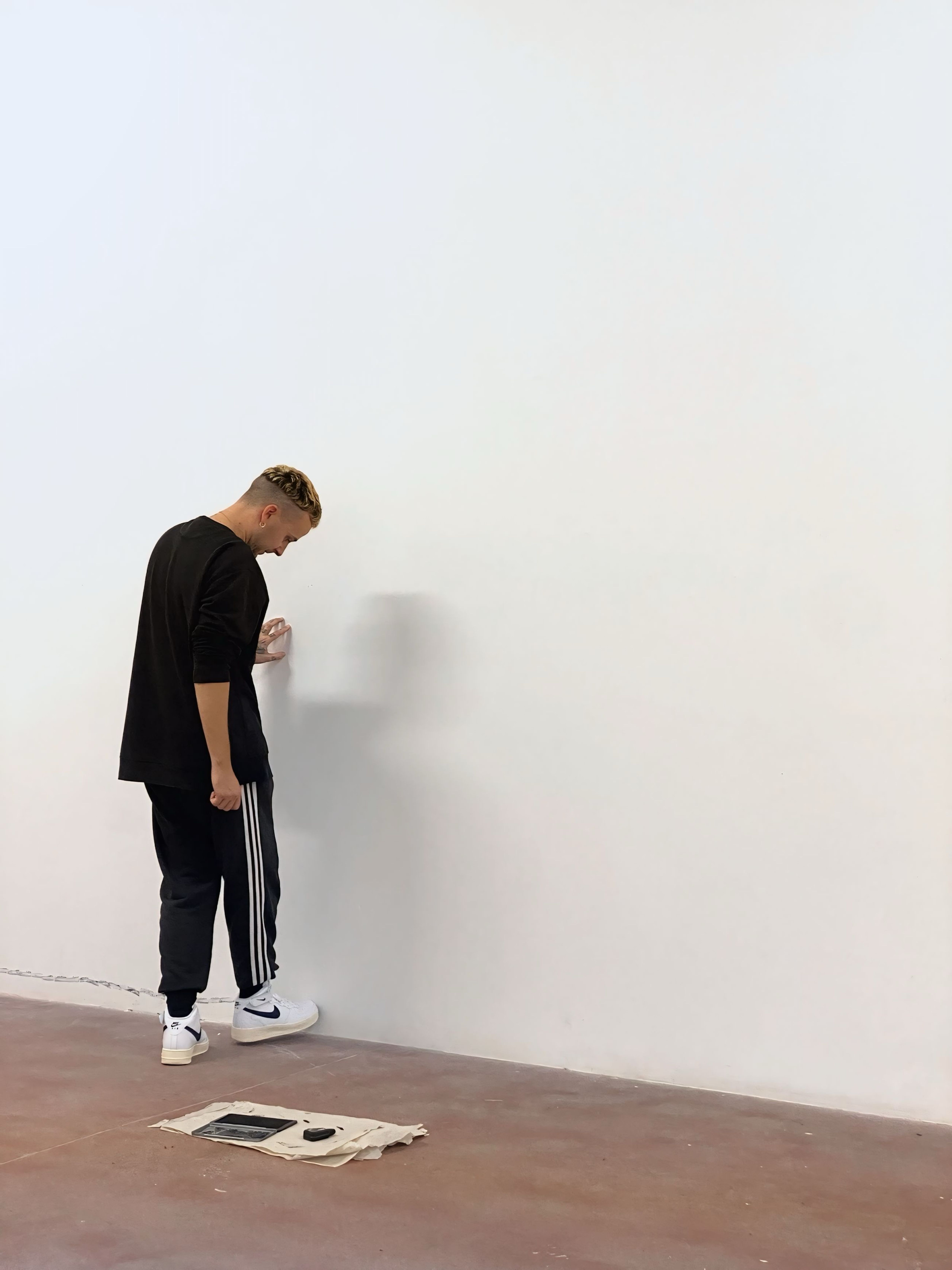 The artist kicking a white wall in a room with a red floor