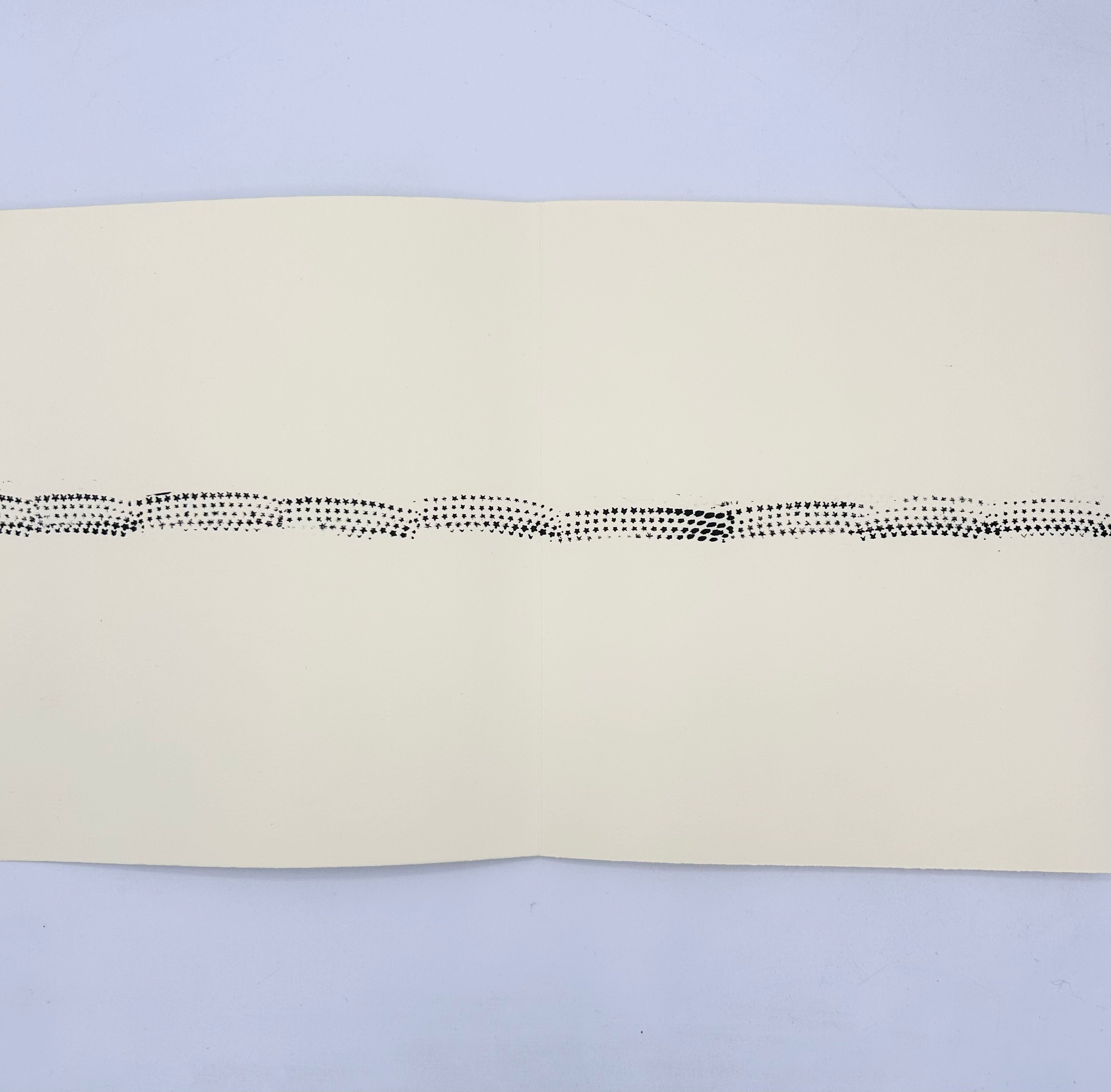 Unfolded leporello book with a line of black star prints across cream paper