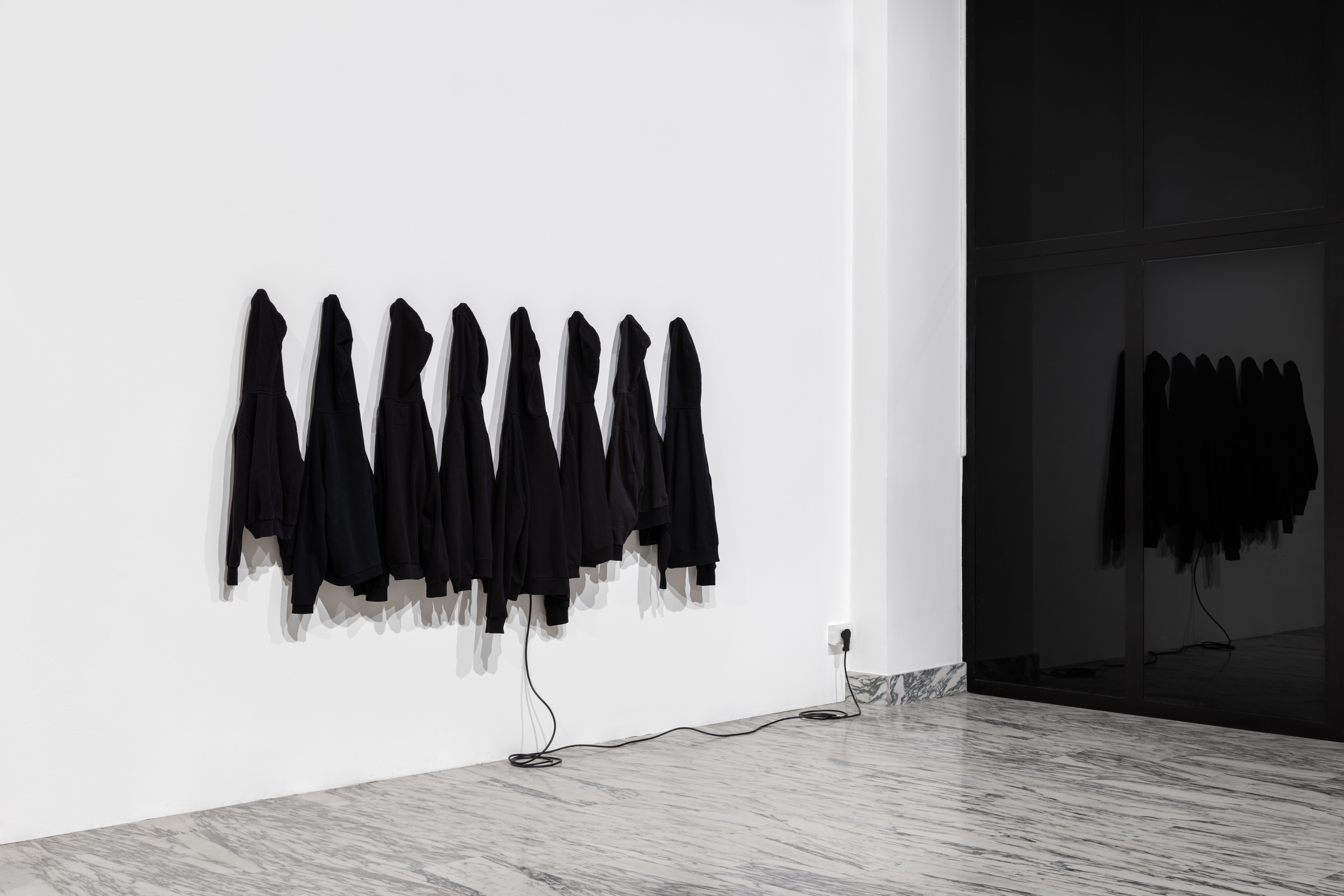 Black sweatshirts on a white wall, reflected in a dark glass panel