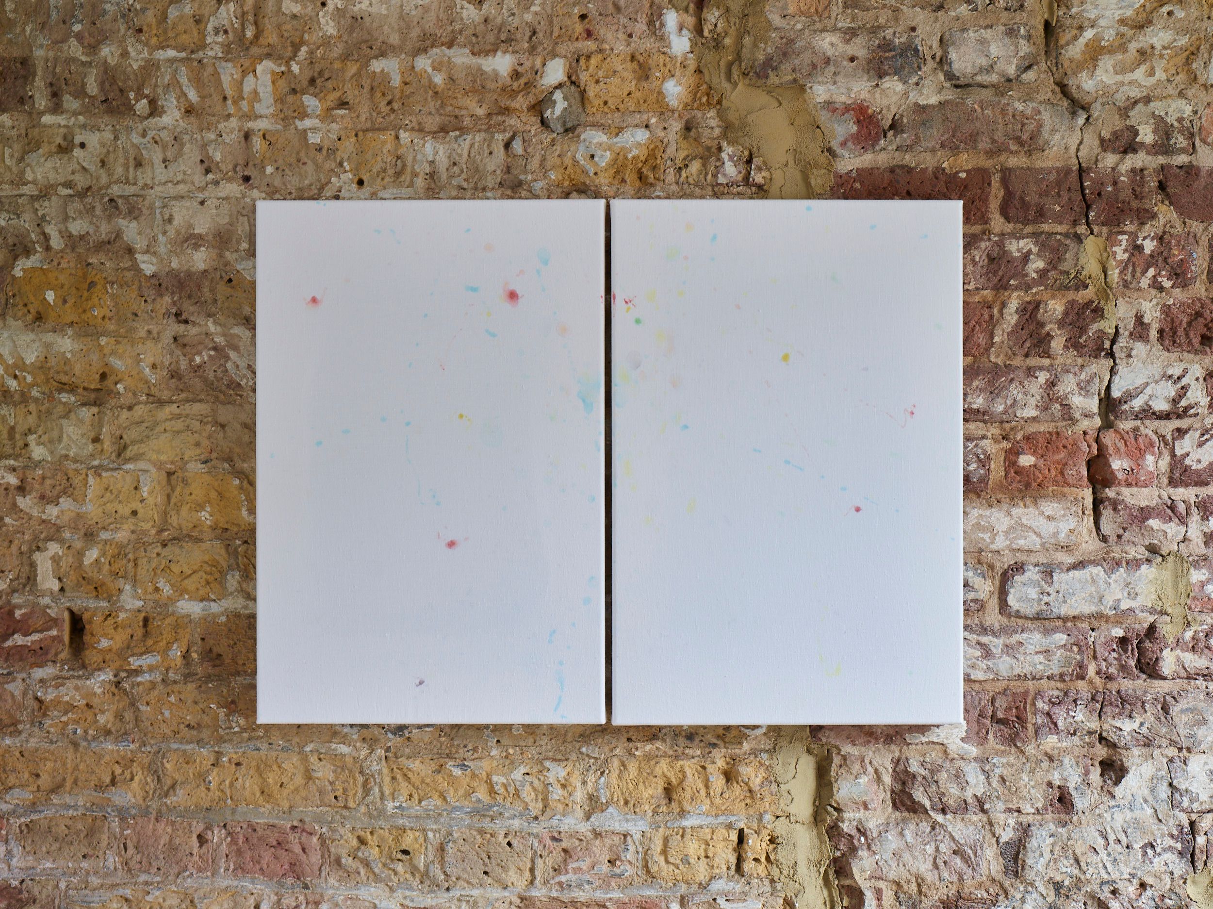 Diptych of white sheets with coloured stains hung on a brick wall