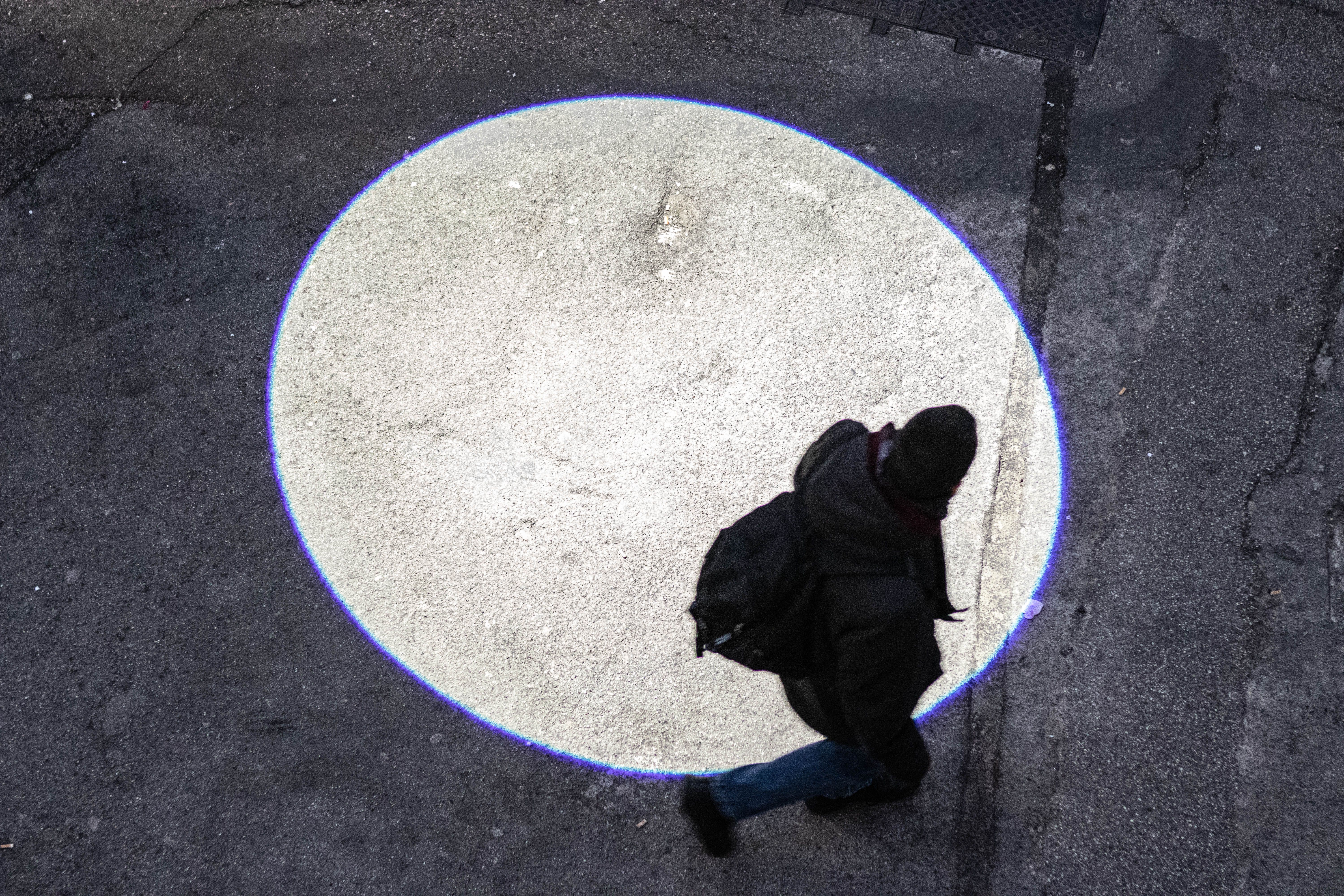 Passer-by walking through a circle of light projected on the pavement