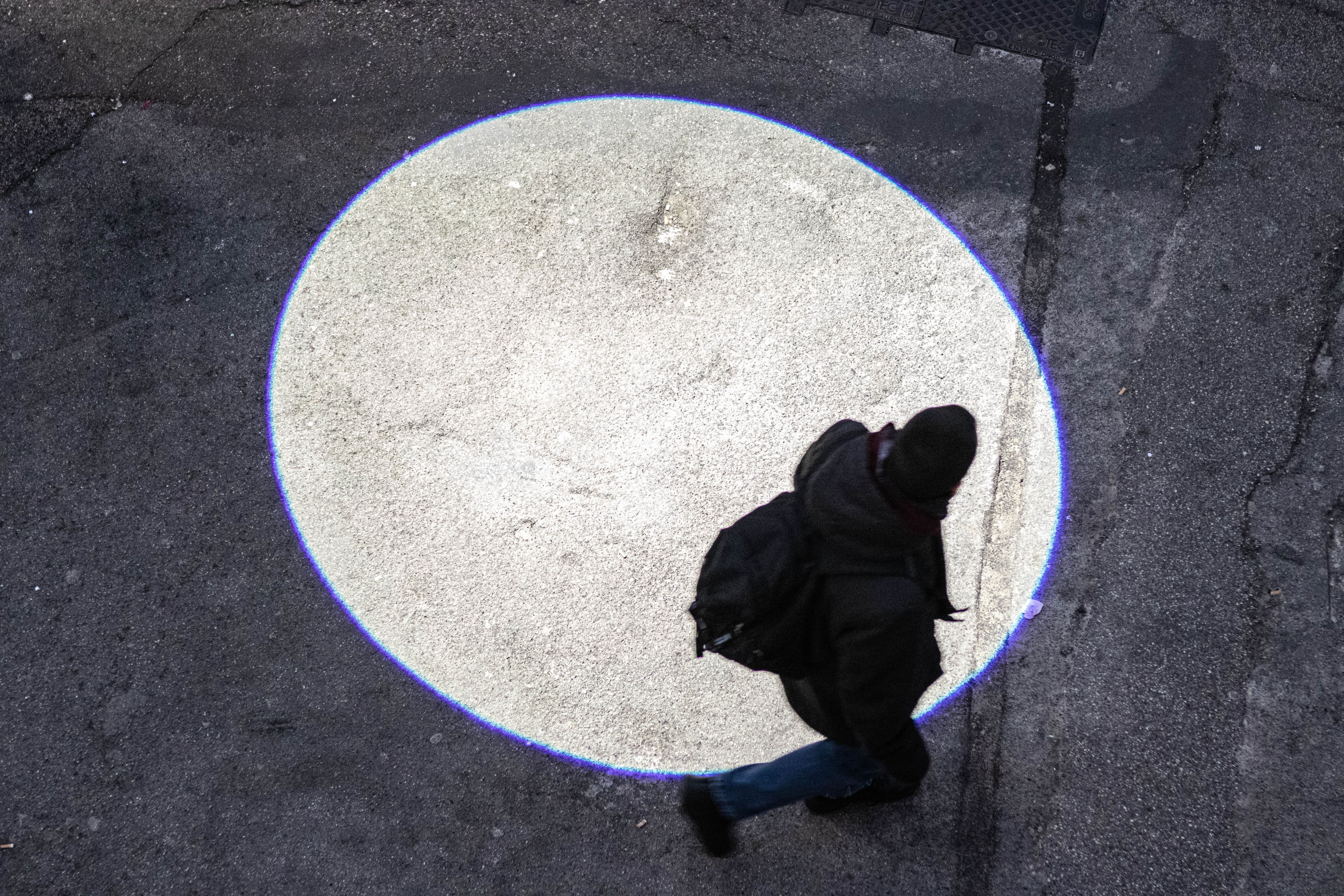 Passer-by walking through a circle of light projected on the pavement