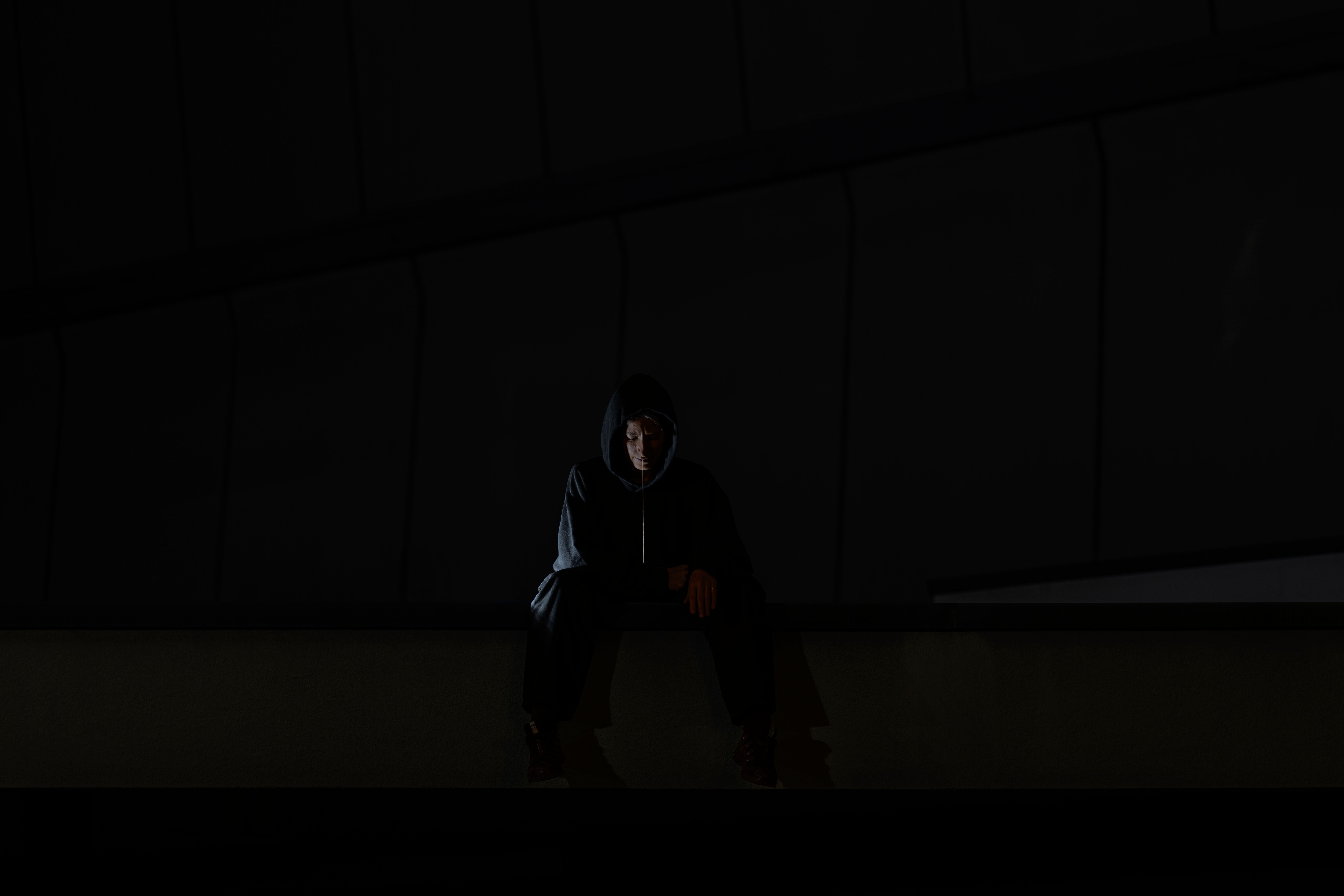 Person in a hood sitting alone on a concrete ledge at night