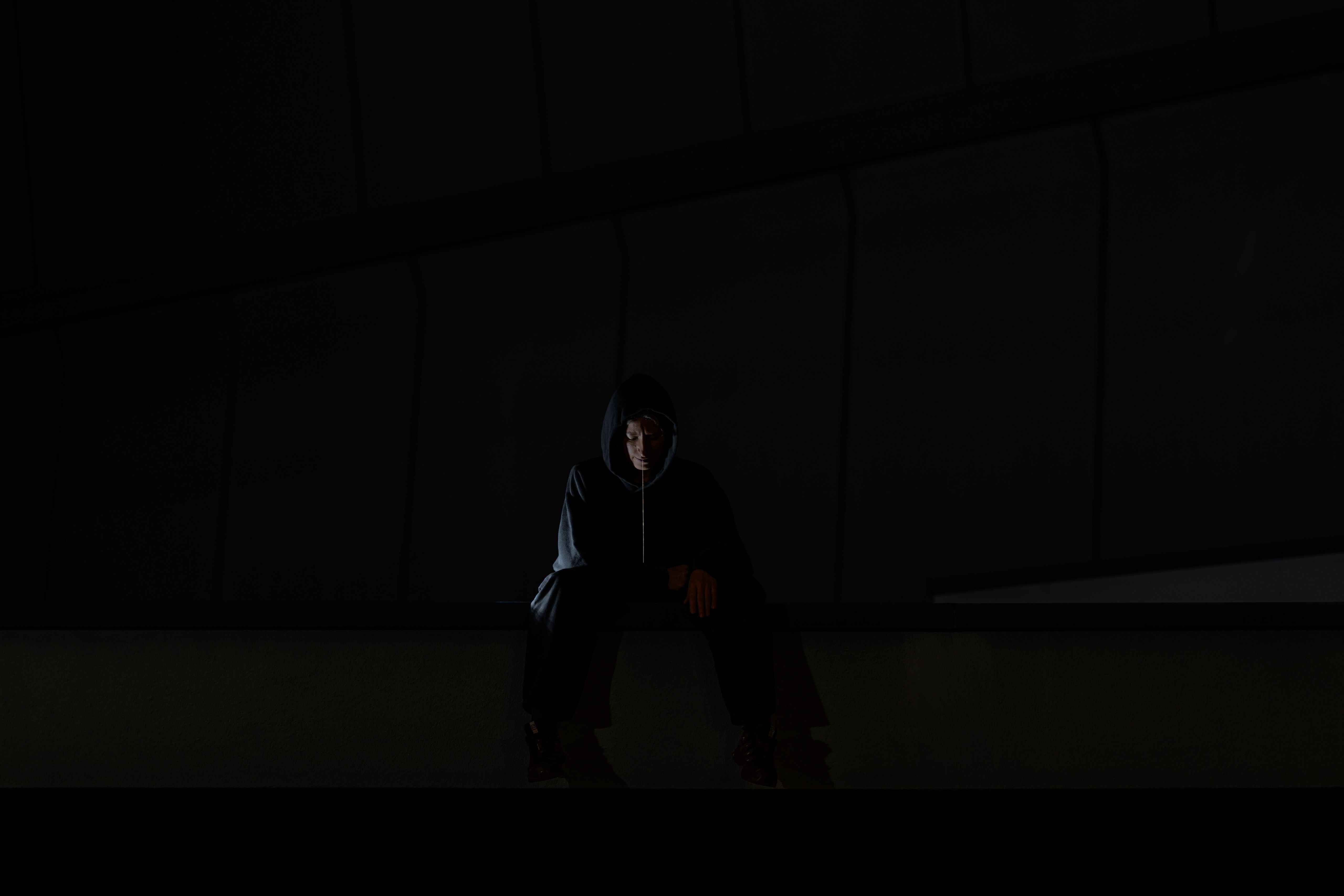 Person in a hood sitting alone on a concrete ledge at night