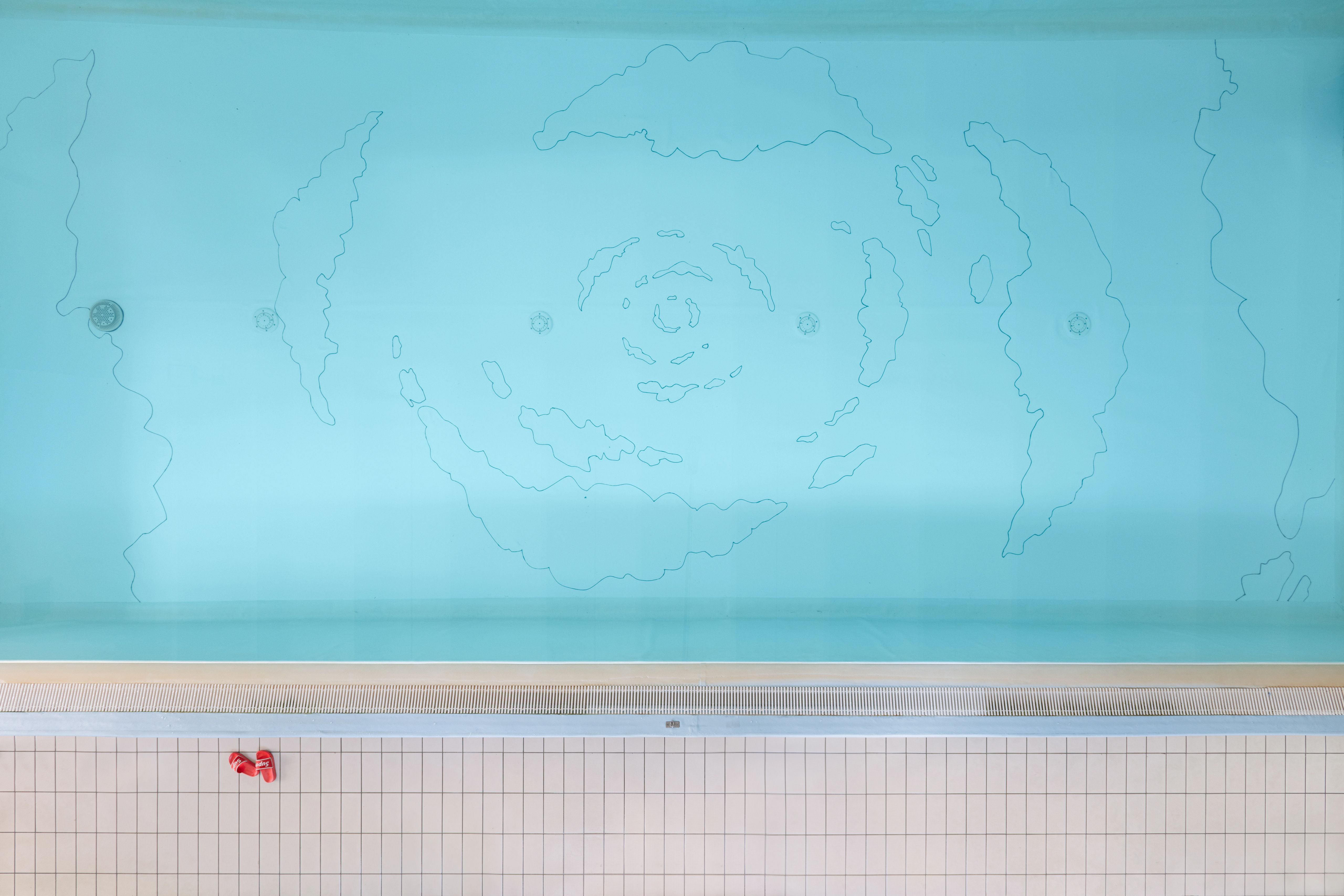 Turquoise pool seen from above, with a drawing of clouds swirling towards the centre on its floor