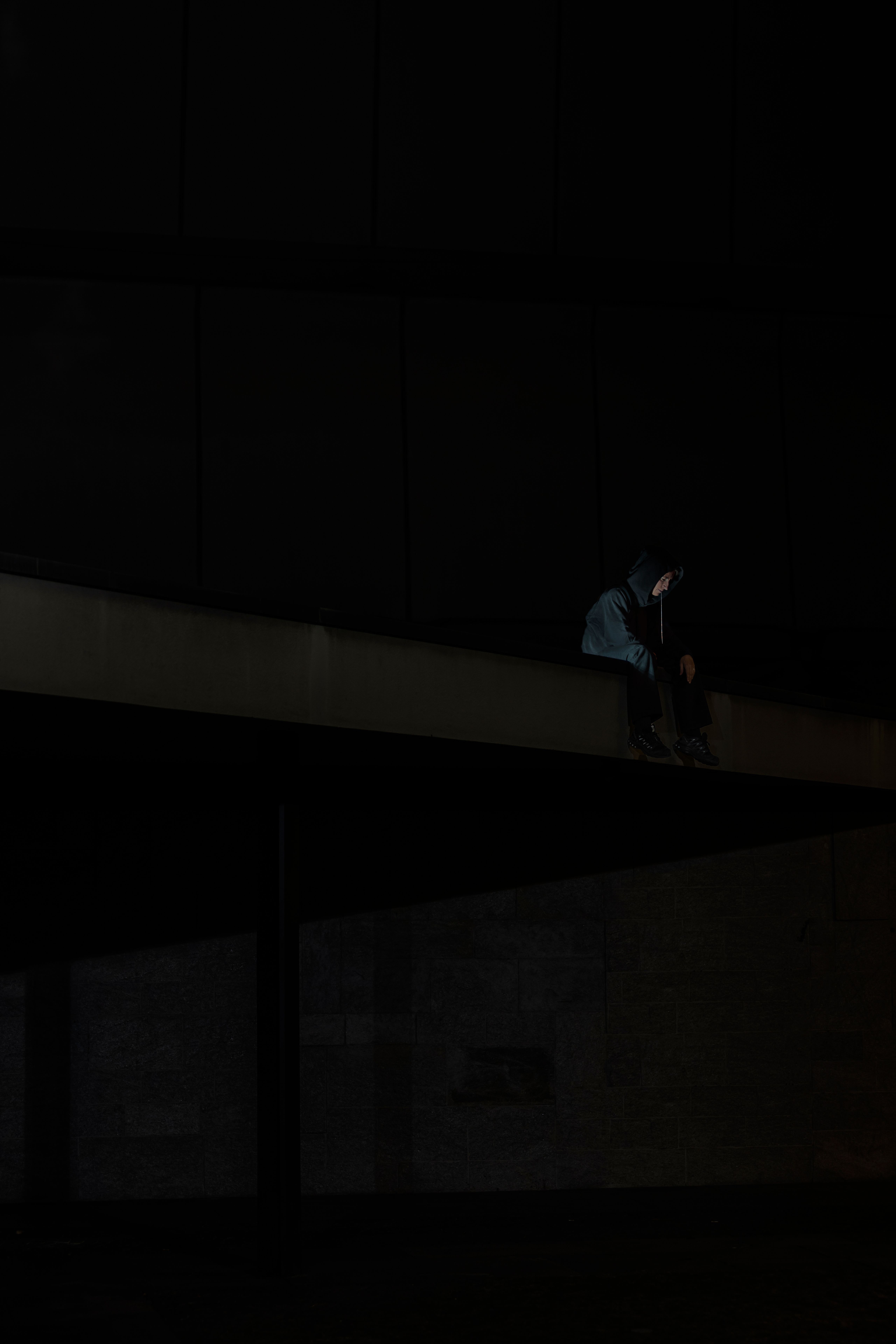 Hooded figure sitting on a ledge of a dark building at night