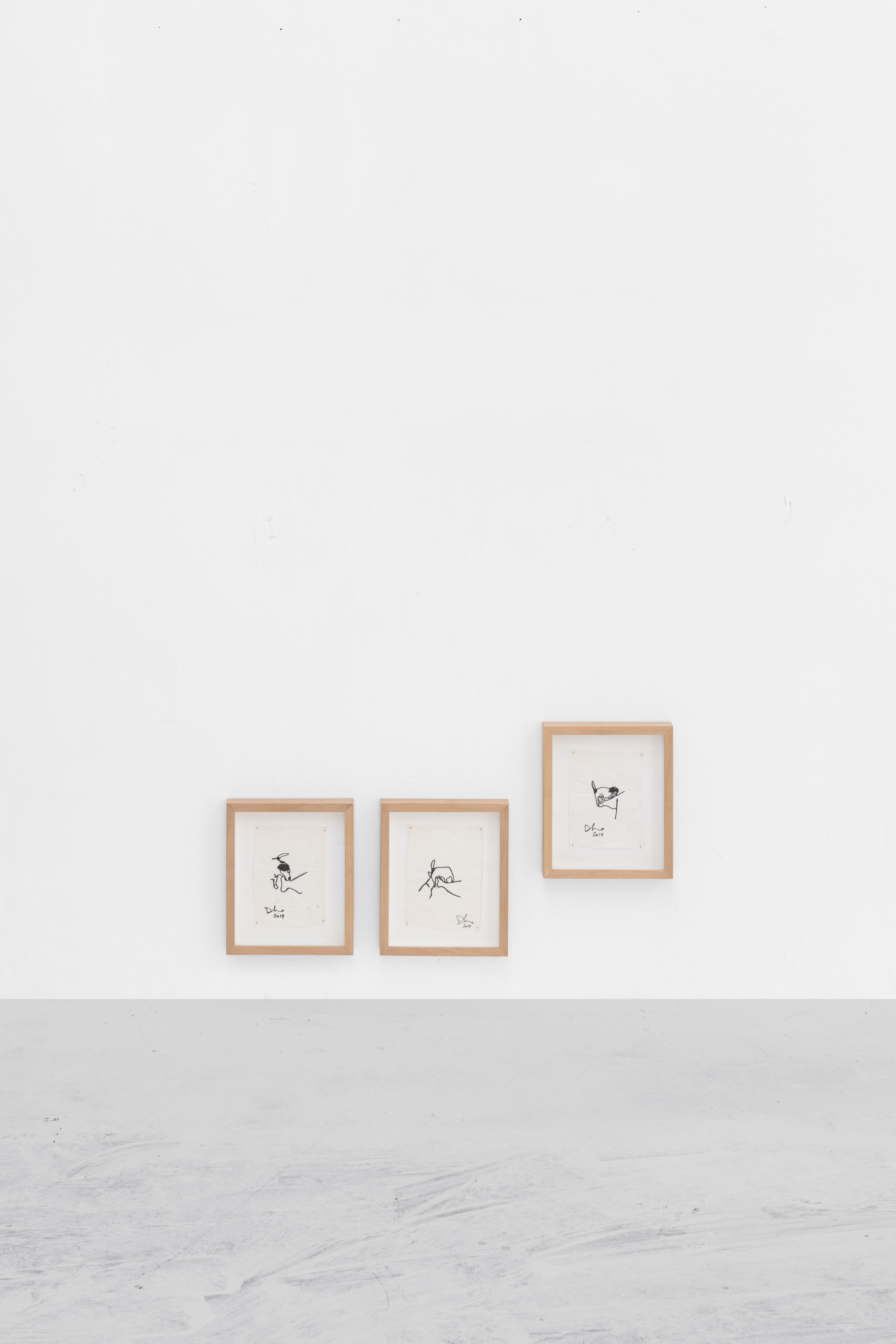 Triptych of small framed ink drawings hung low on a white wall