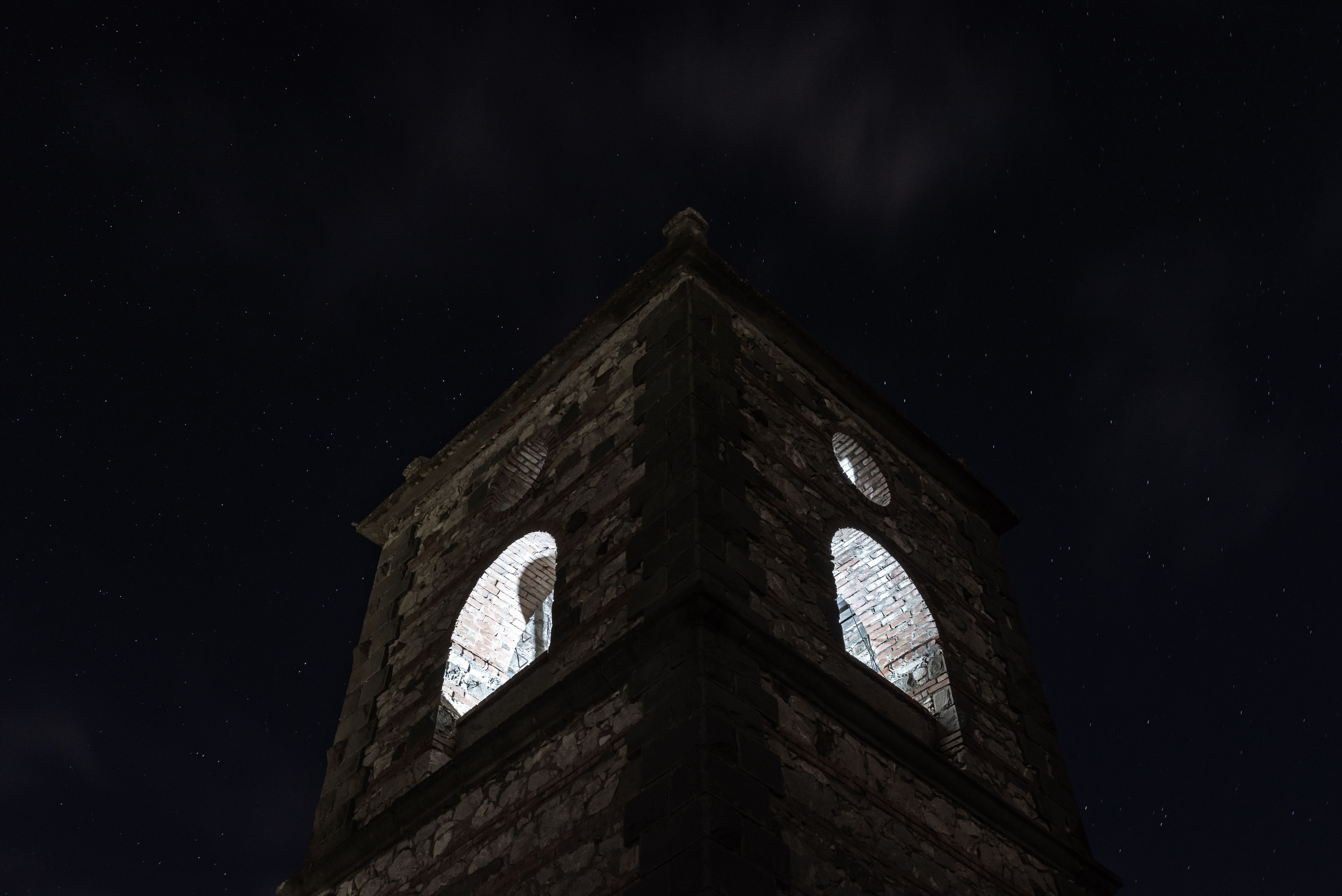 Stone bell tower at night seen from below, its arched openings lit white