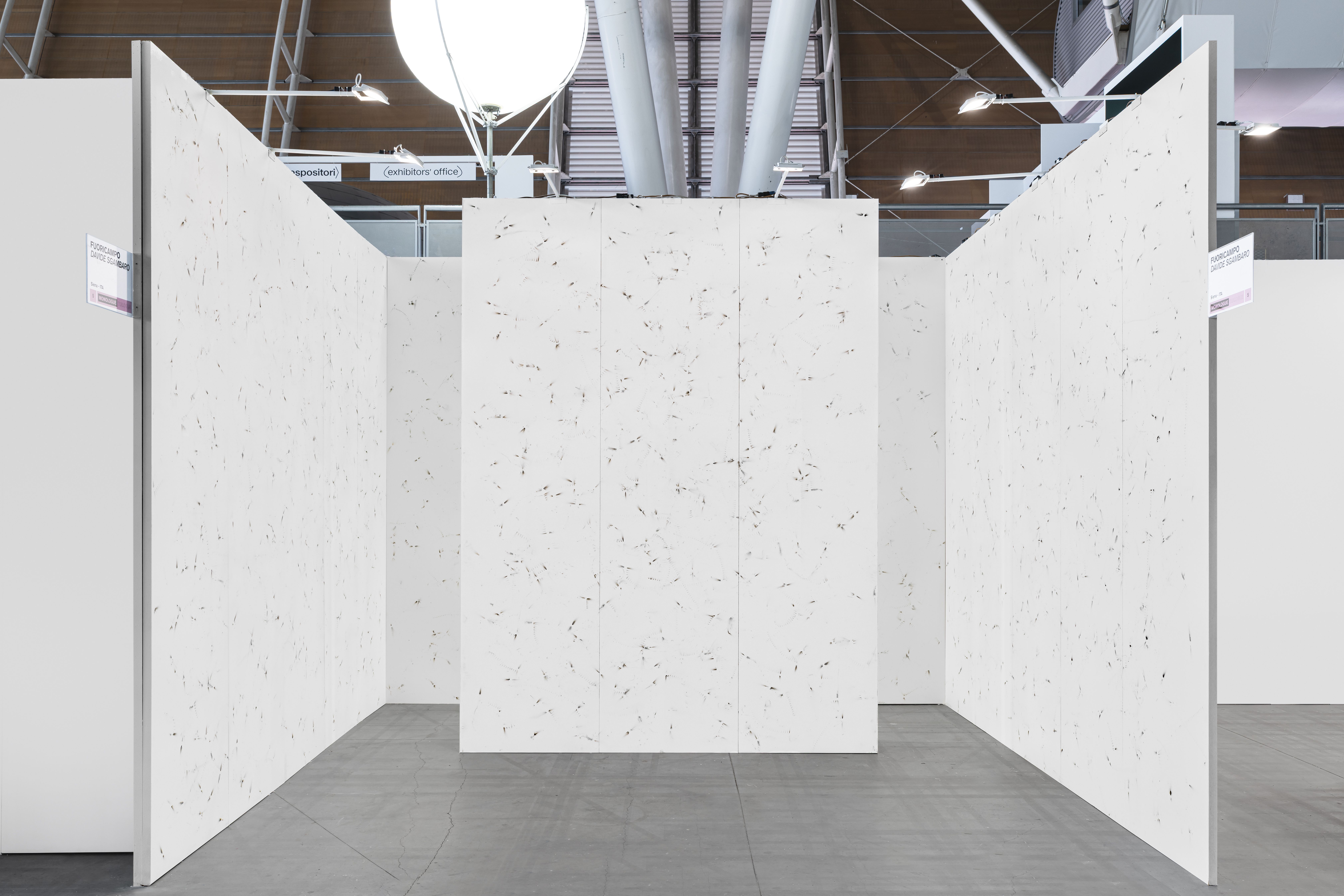 White exhibition booth with walls covered in small burn marks