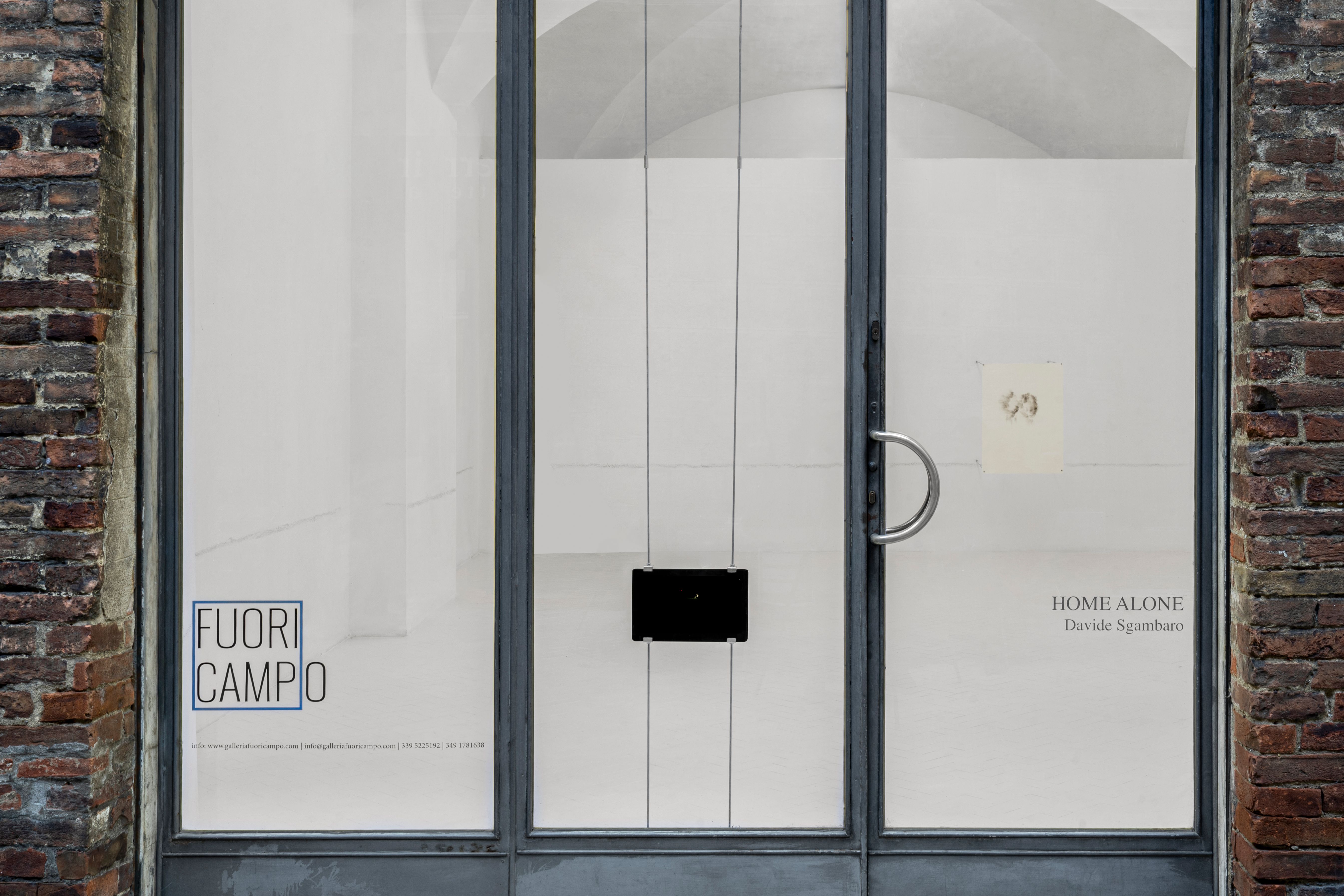 Gallery shop window with a tablet showing the video and the HOME ALONE exhibition lettering