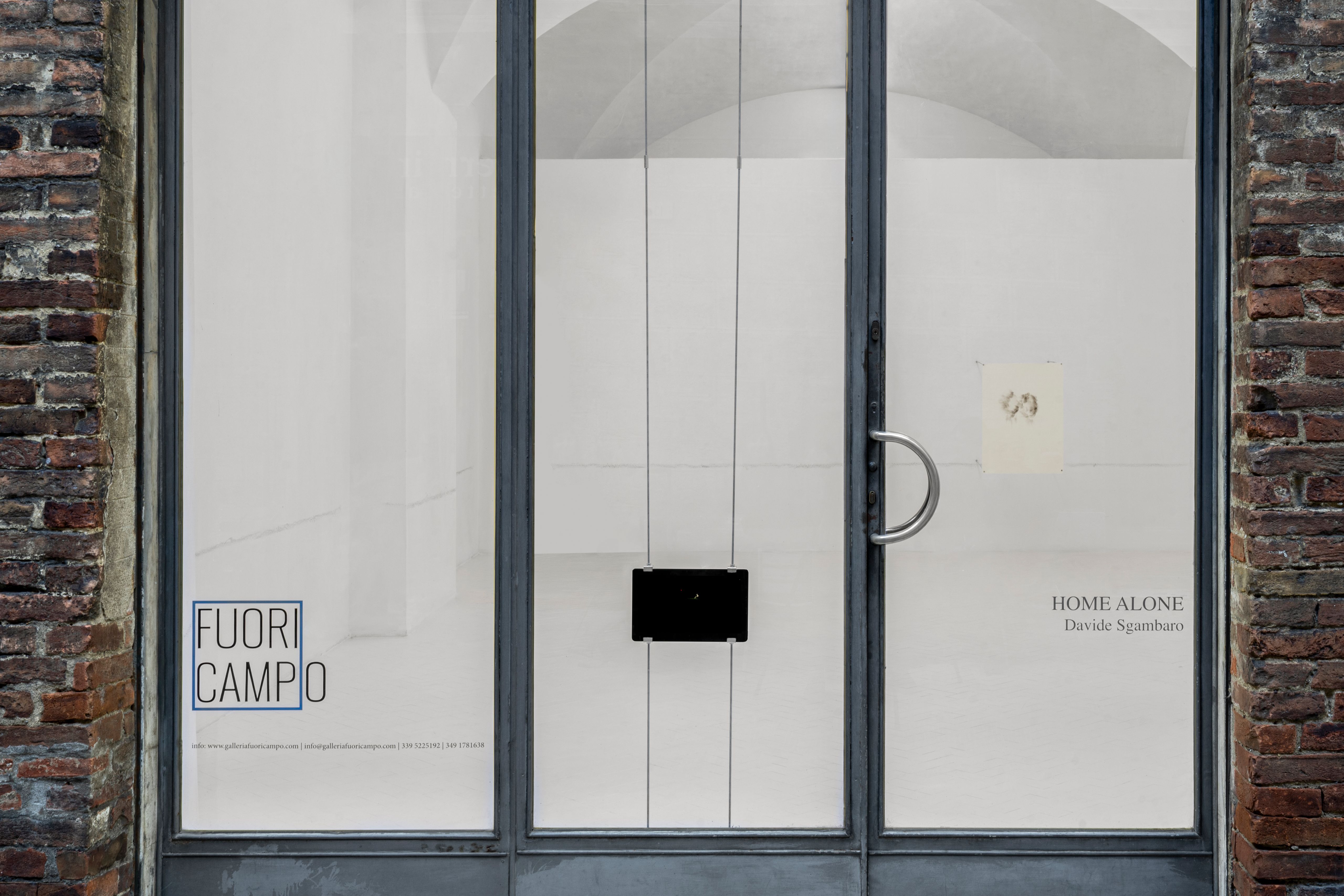 Gallery shop window with a tablet showing the video and the HOME ALONE exhibition lettering