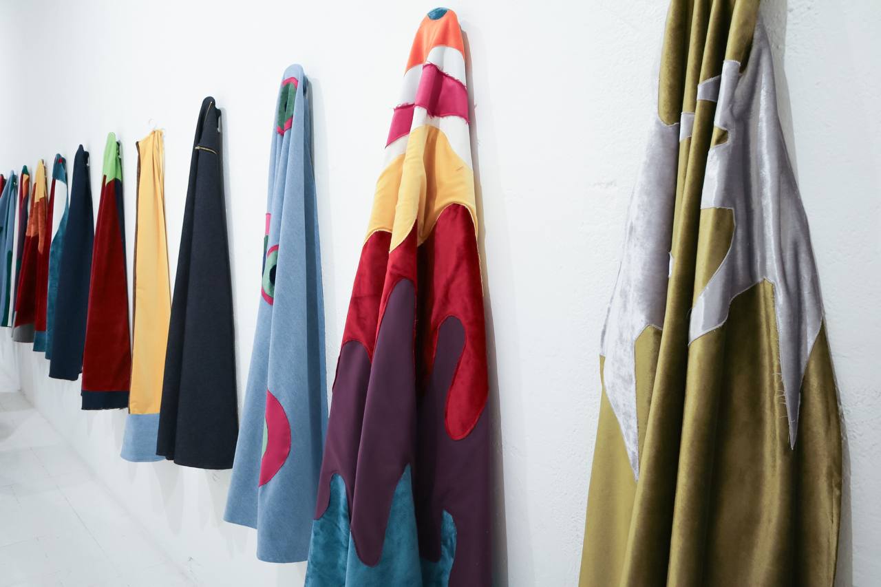 Row of colourful superhero capes hanging along a white wall, seen up close