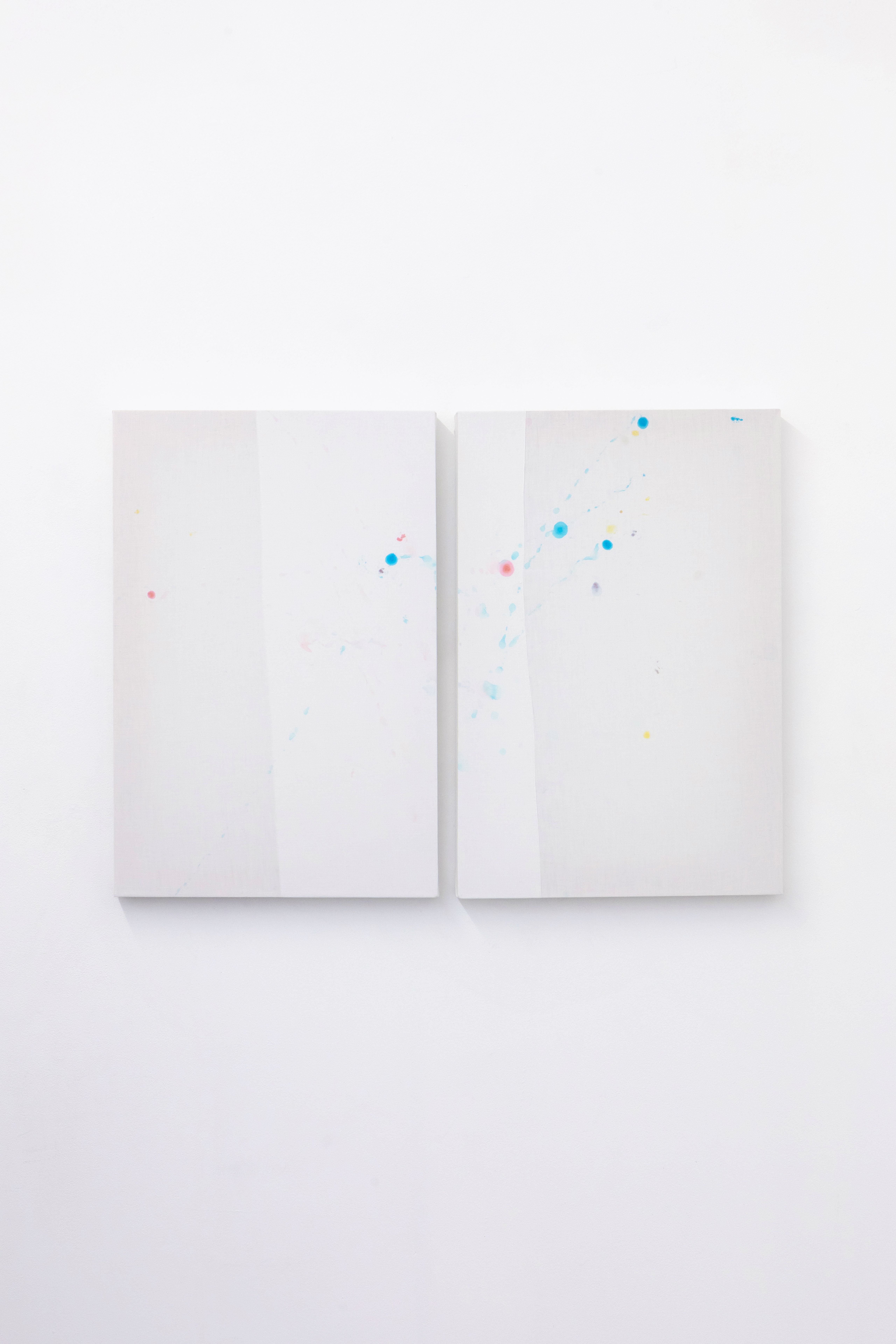 Diptych of white sheets with small coloured stains on a white wall