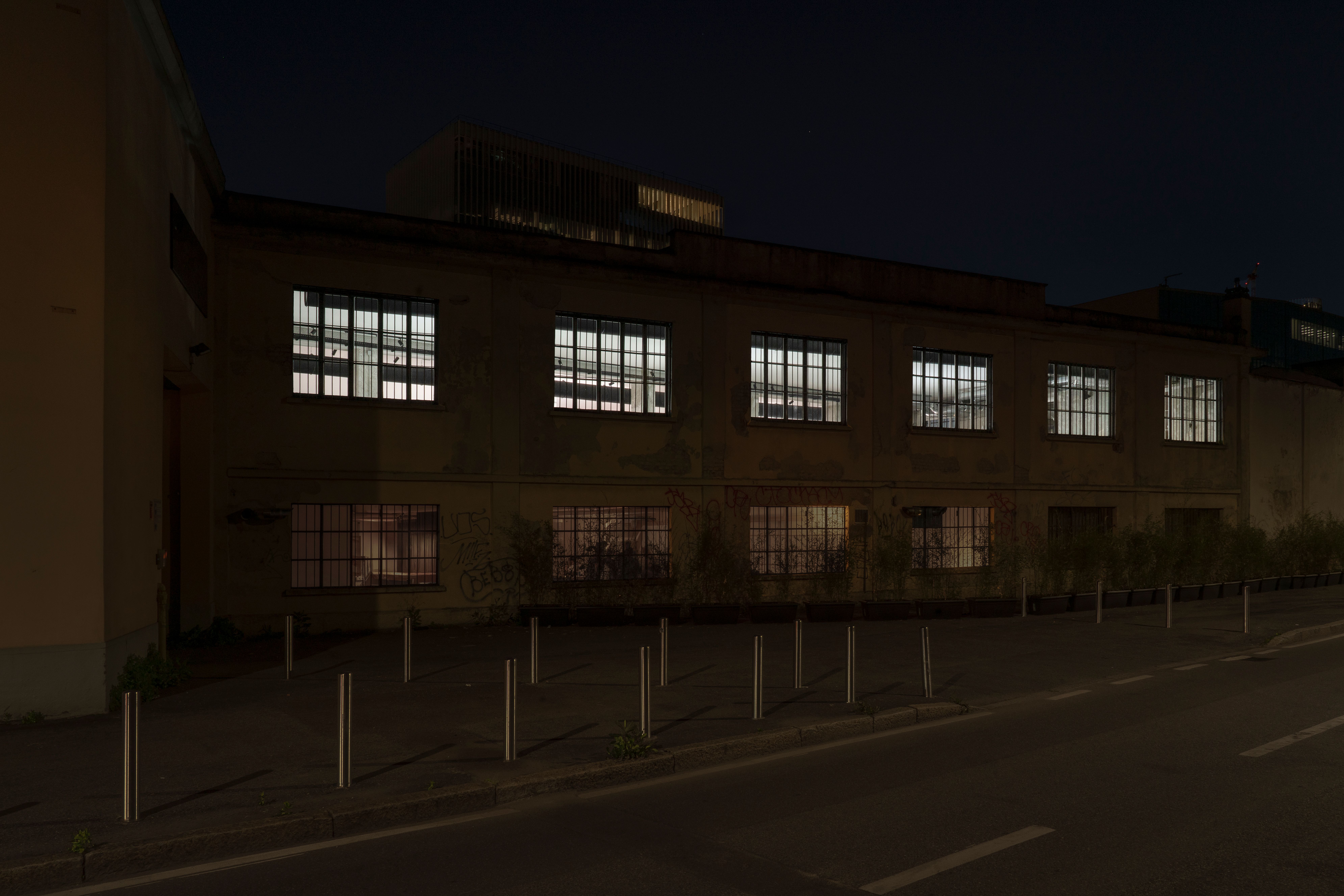 Industrial building at night seen from the street, its windows lit by strobe lights