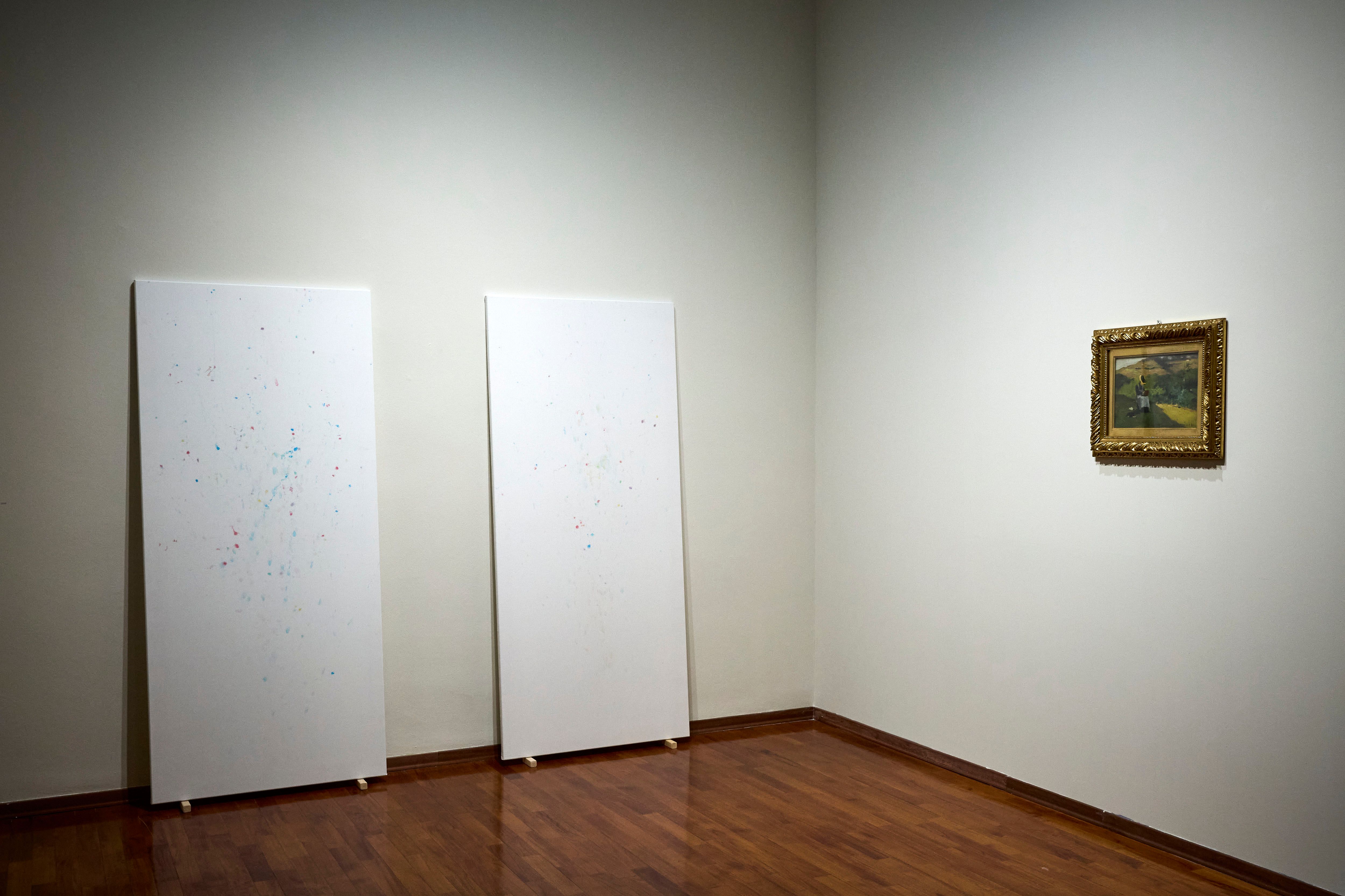 Two tall white sheets leaning against a gallery wall next to a framed painting