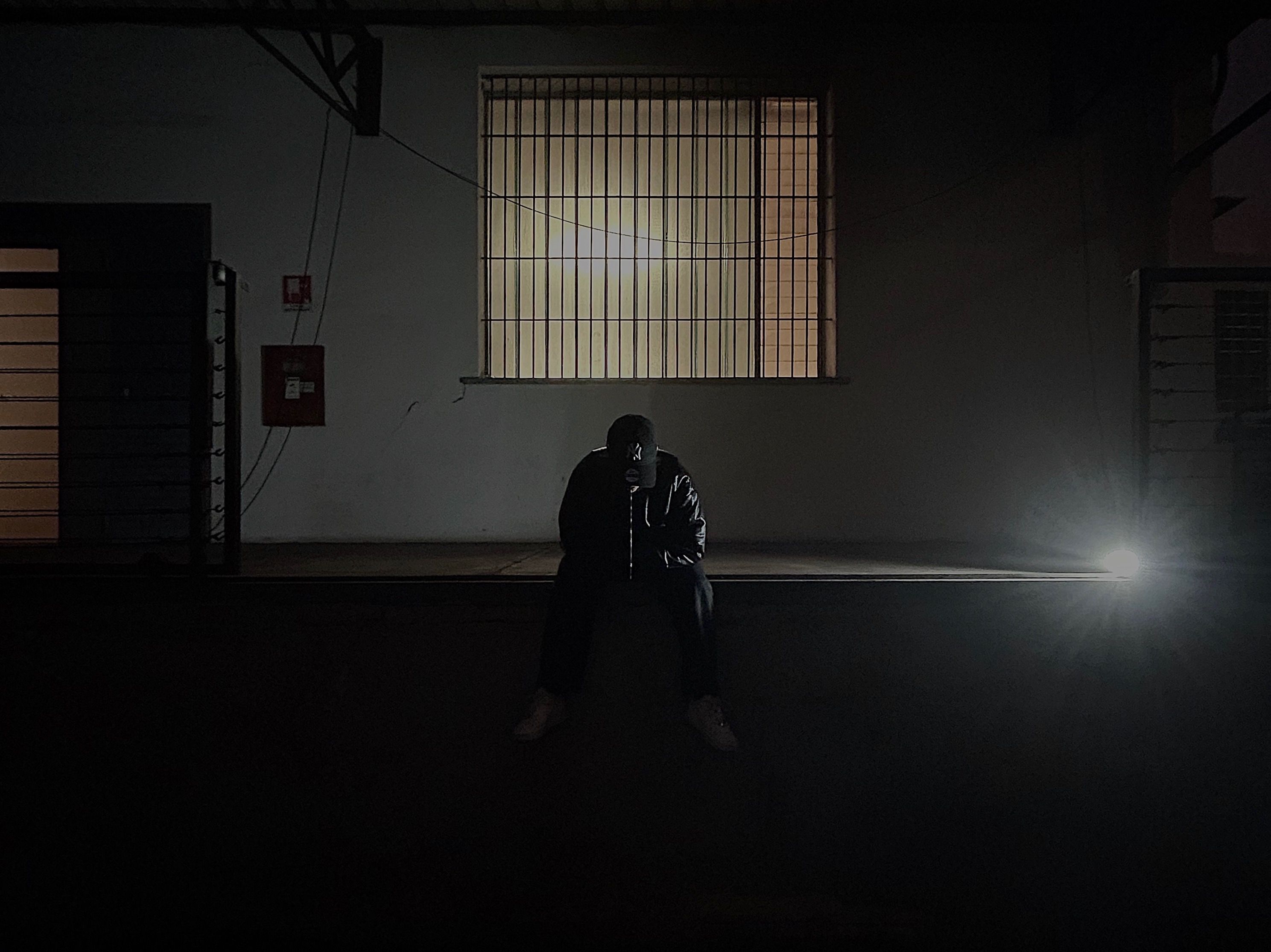Person sitting in a dark courtyard with a silver thread hanging from the mouth