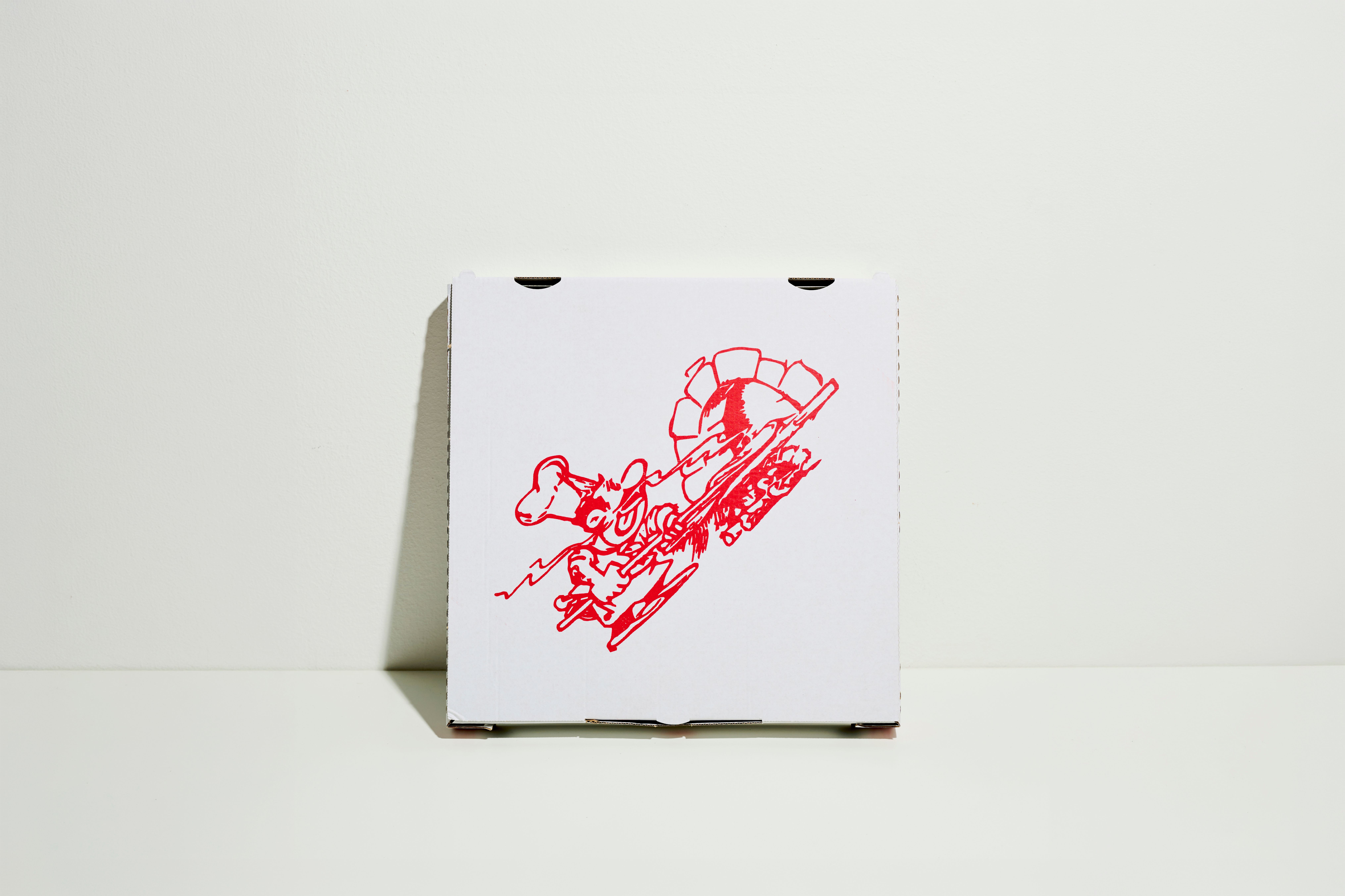 Pizza box printed with a red drawing, leaning against a white wall