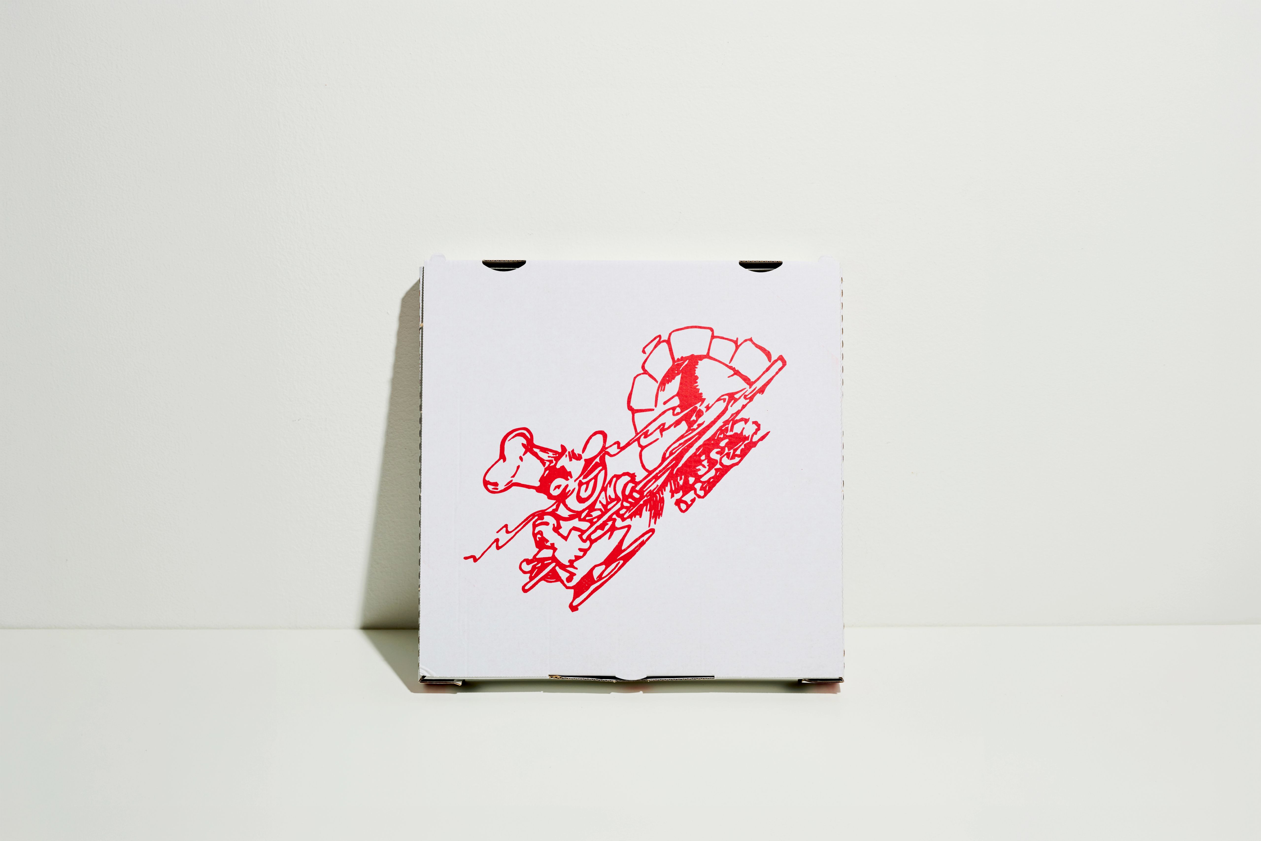 Pizza box printed with a red drawing, leaning against a white wall