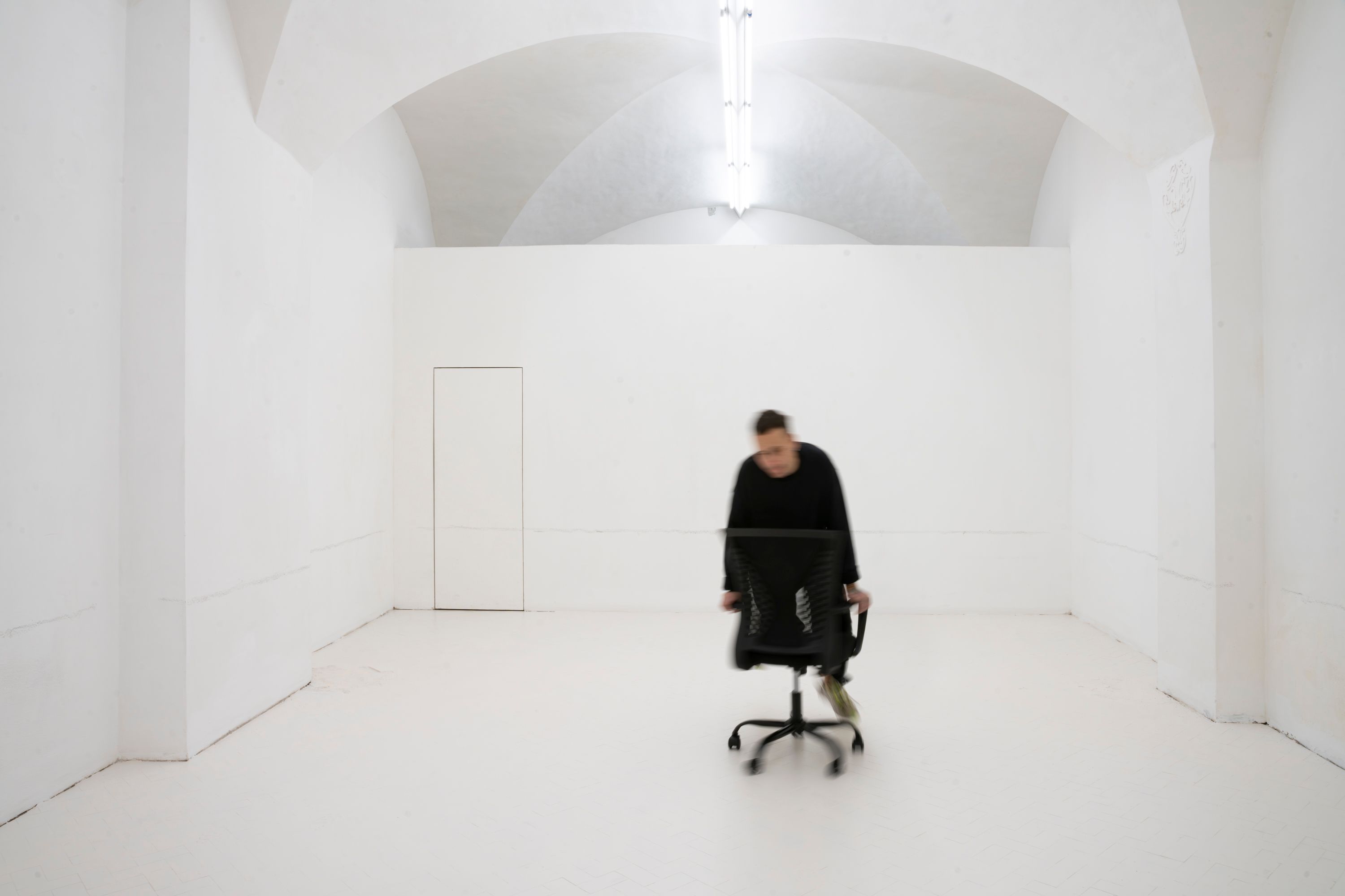 The artist on an office chair in a white vaulted gallery room