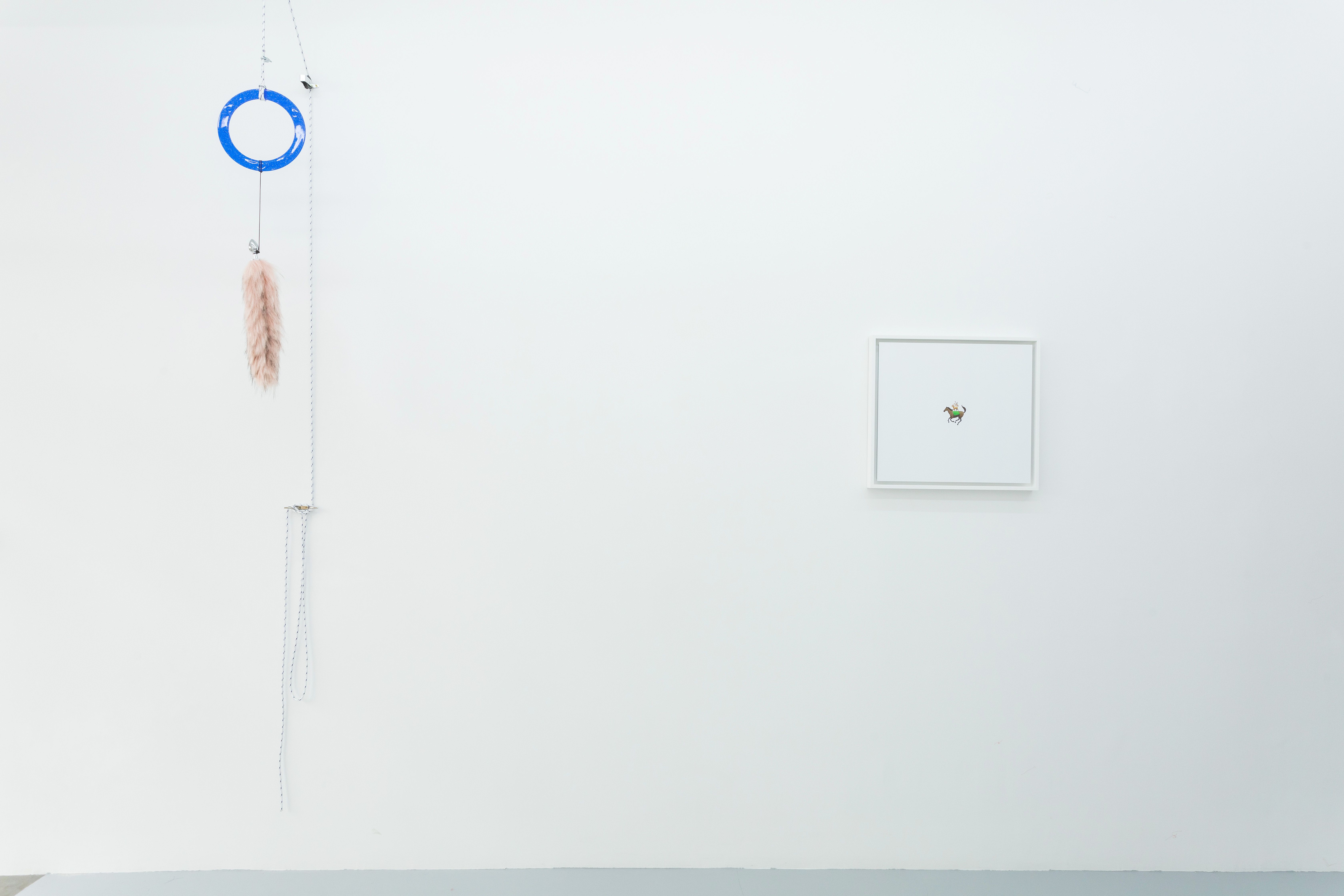 Gallery wall with a small framed drawing and a hanging piece with a blue ring and pink tassel