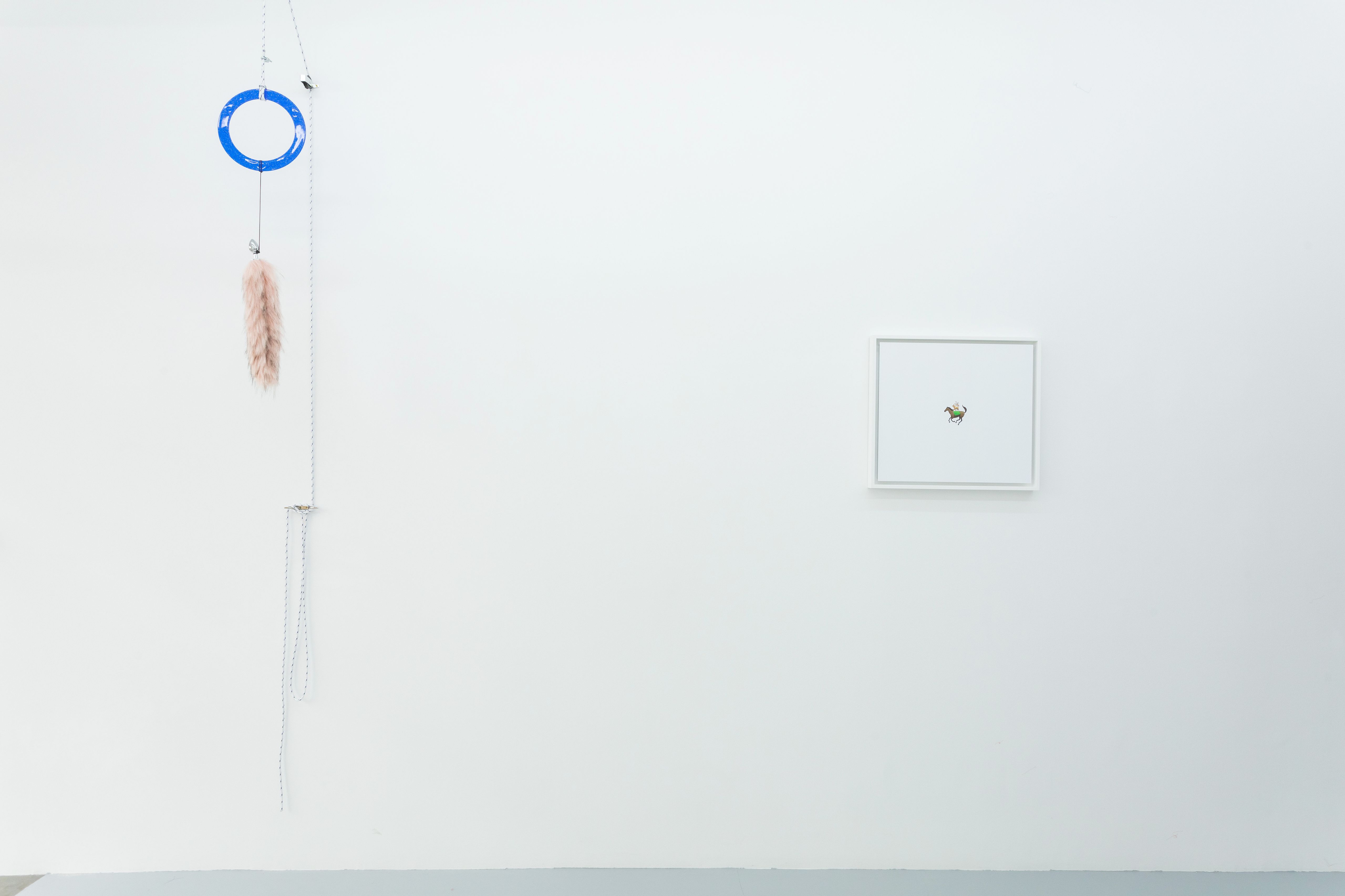 Gallery wall with a small framed drawing and a hanging piece with a blue ring and pink tassel