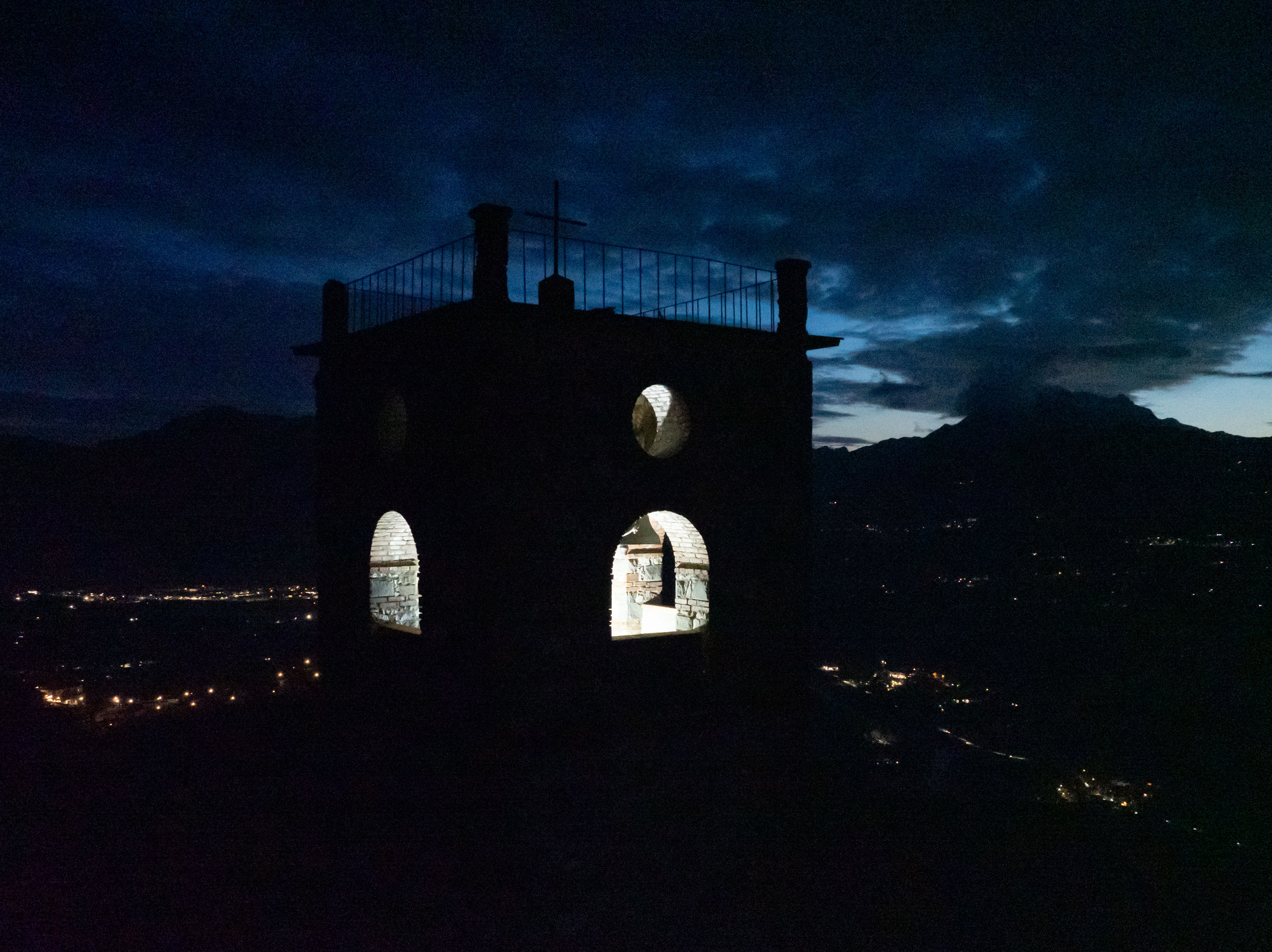 Bell tower silhouetted at dusk above a valley, its openings lit white