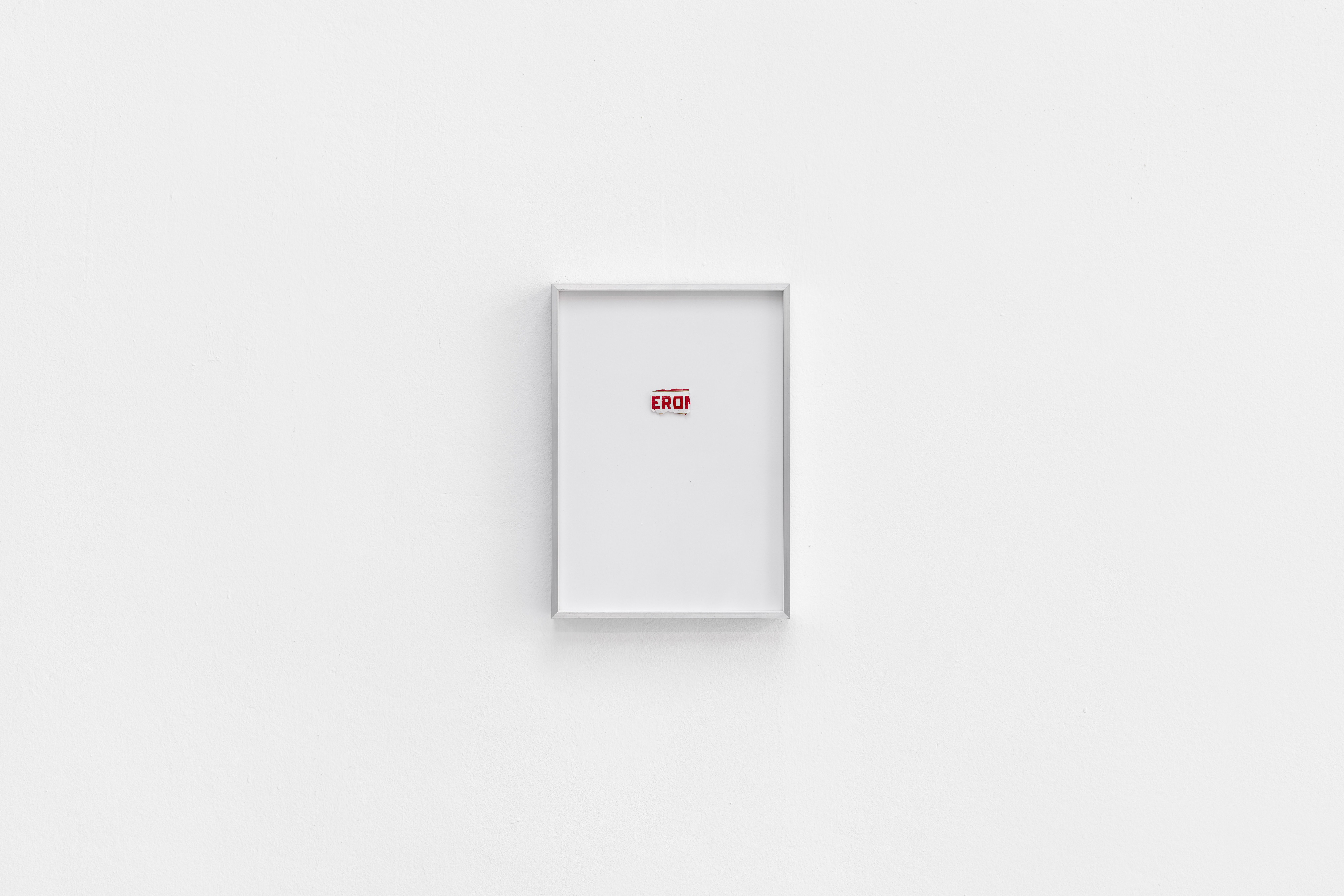 Small aluminium frame on a white wall holding a torn fragment of a beer label reading EROI
