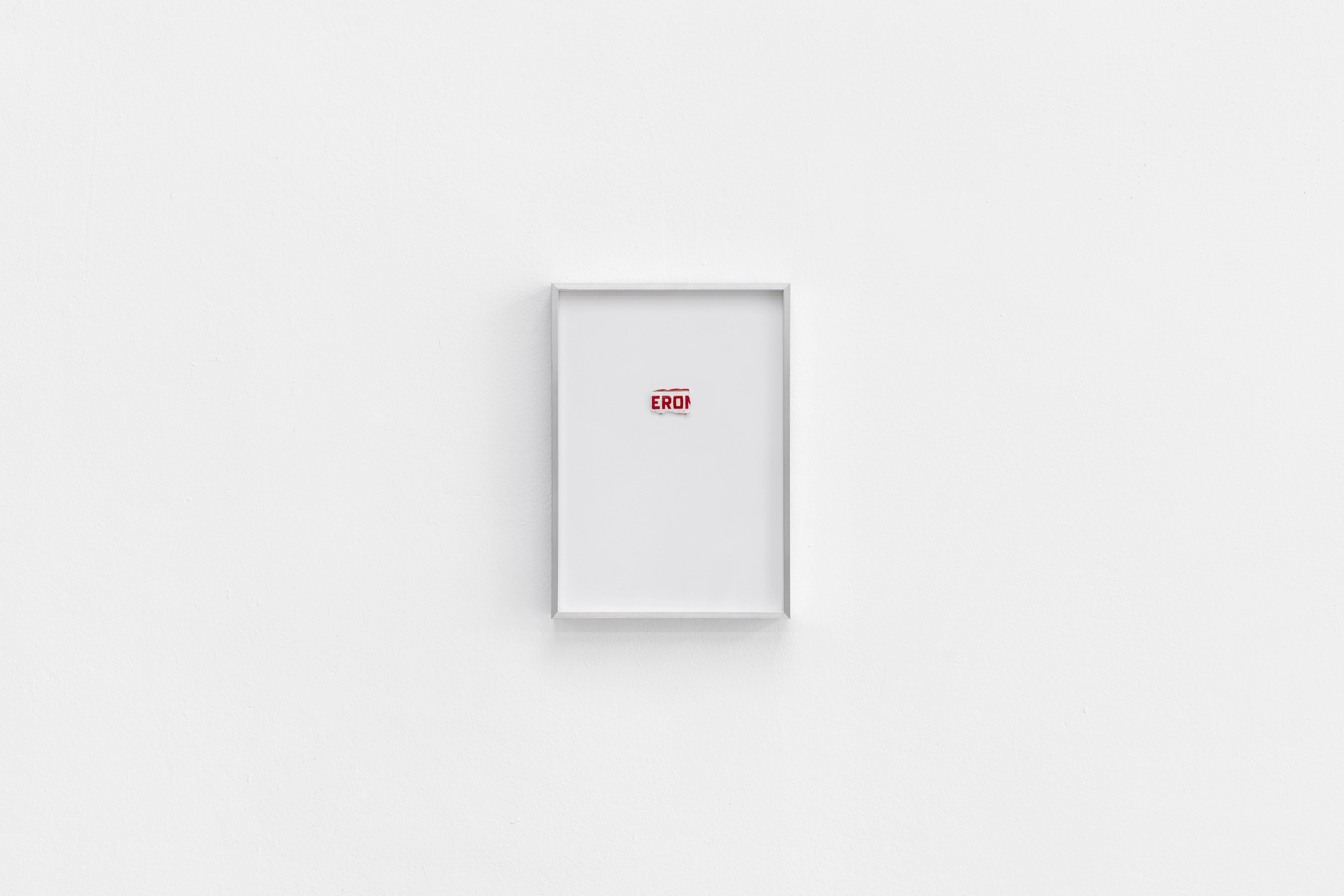 Small aluminium frame on a white wall holding a torn fragment of a beer label reading EROI